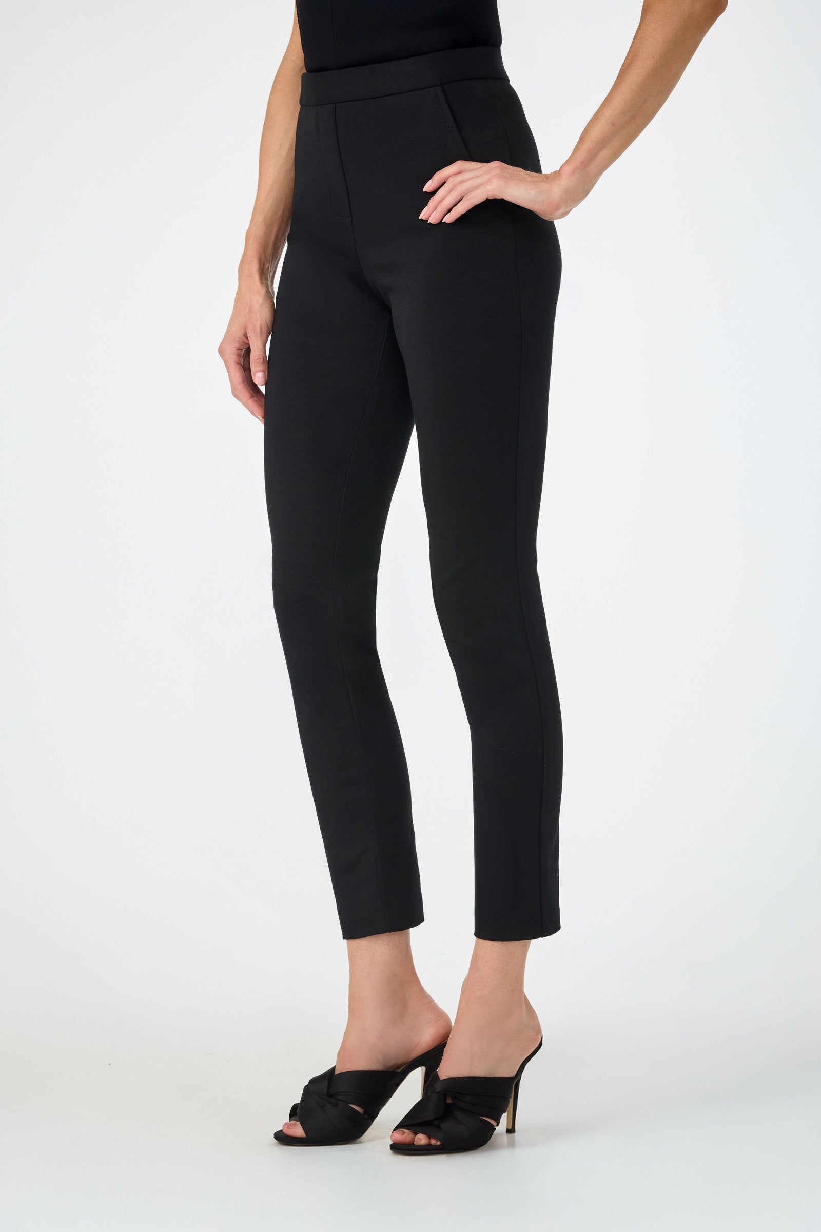 A woman stands with one hand on her hip in Honey Straight Leg Pants and black heeled sandals against a plain white background. Her upper body is partially out of frame.