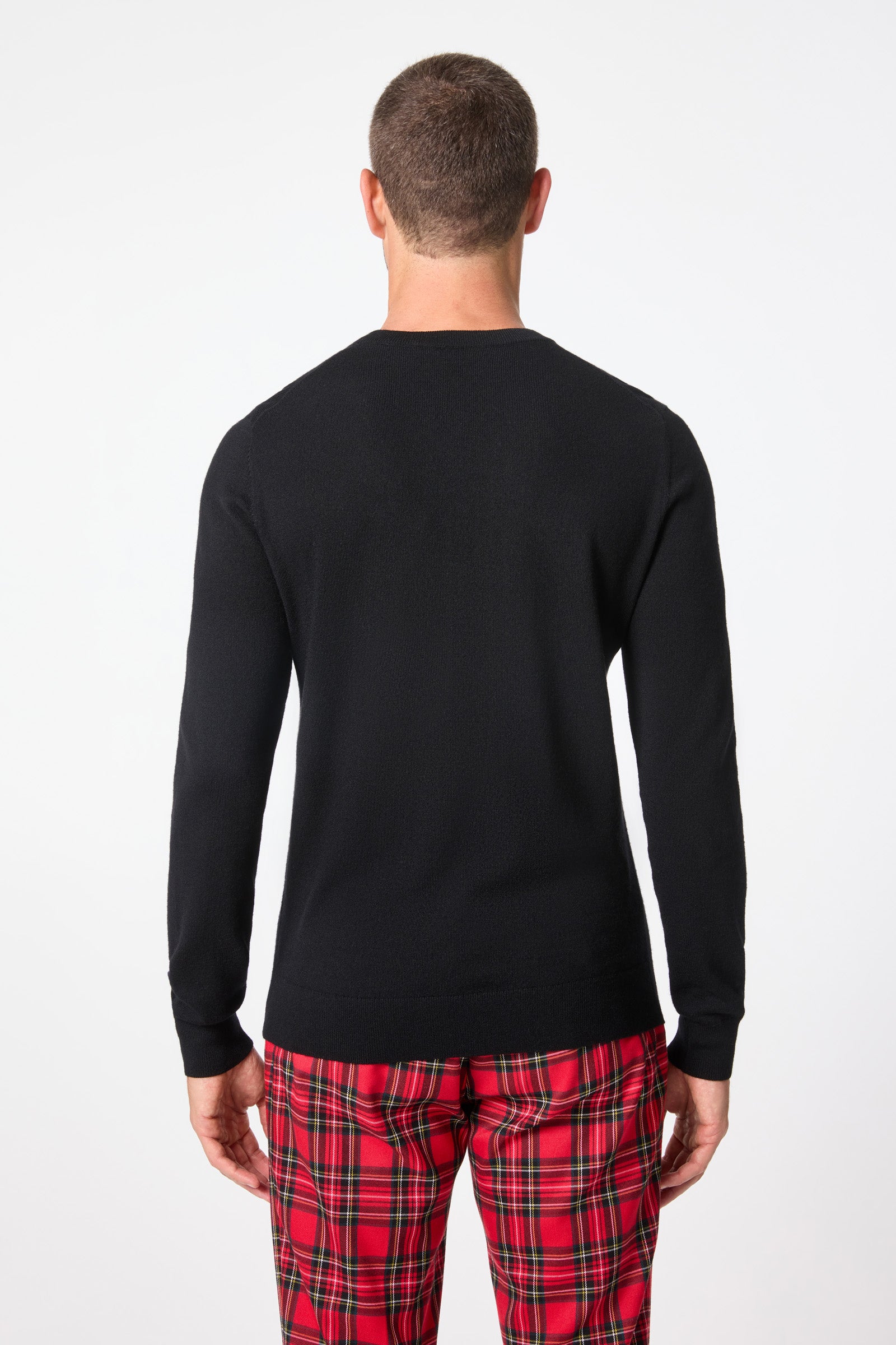 A man with short hair stands facing away from the camera, wearing a black Martini Crewneck Sweater and red plaid pants against a plain white background.