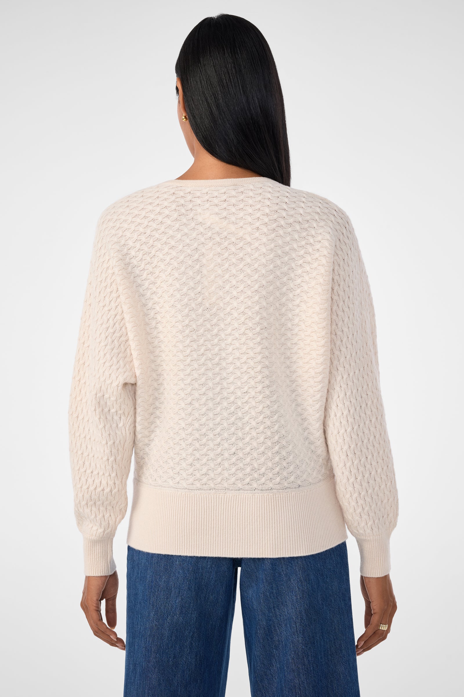 A person with long dark hair, viewed from behind, wears the Lima V-Neck Pullover in cream and blue denim jeans, standing against a plain light background.