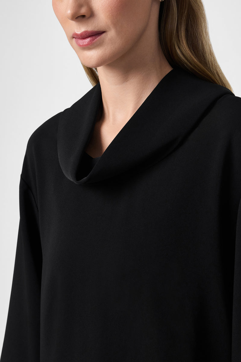 A woman models the Staged Top, a black cowl-neck style. She is shown from the shoulders up, with only the lower half of her face visible against a plain white background.