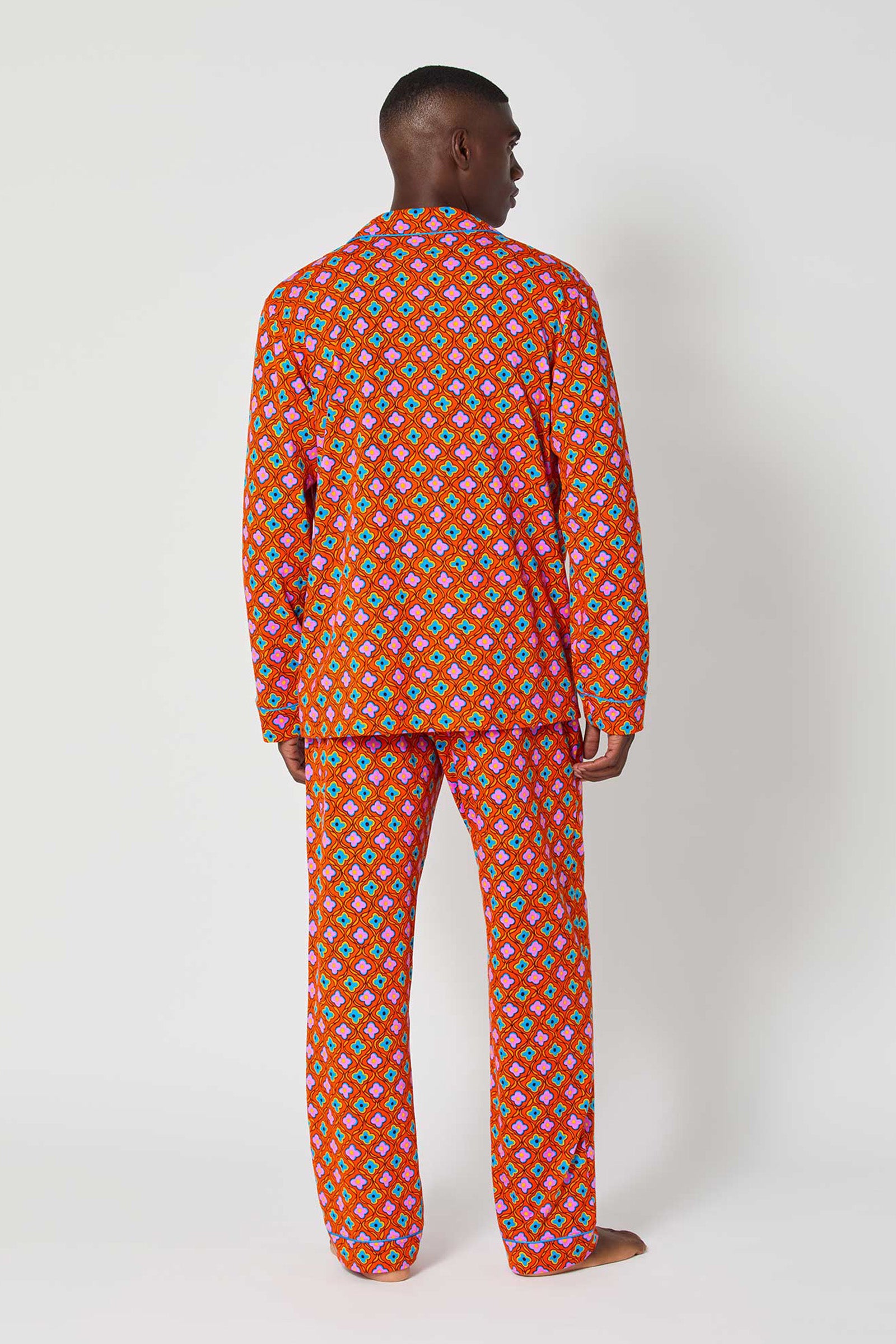 A person faces away, wearing the Daisy Foulard Mens Classic Pj—a long-sleeve red pajama set with a vibrant multicolored geometric print—against a plain white background.