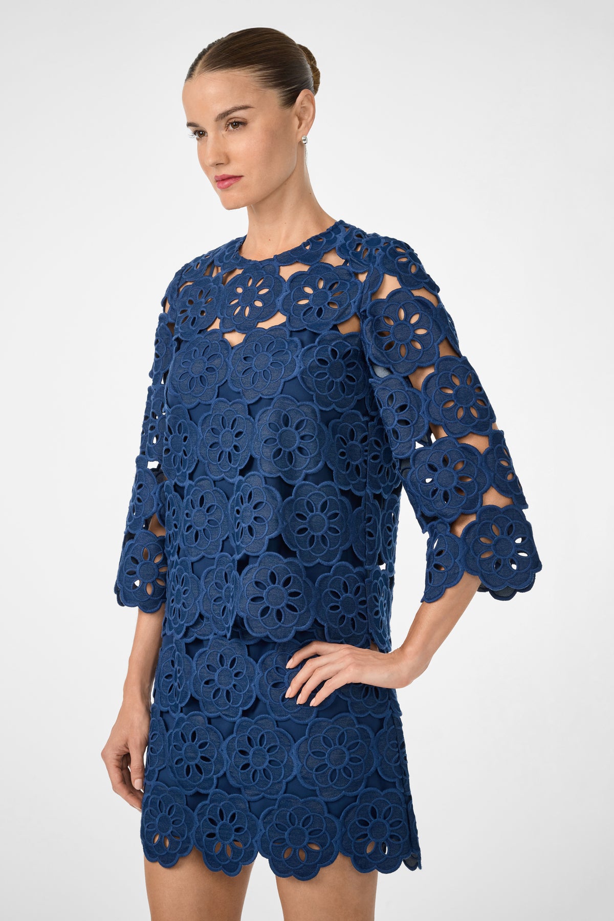 Woman wearing the Kabosu Top with Kusho embroidery, featuring large floral lace cutout patterns, three-quarter sleeves, and scalloped edges, standing with one hand on her hip against a plain light background.