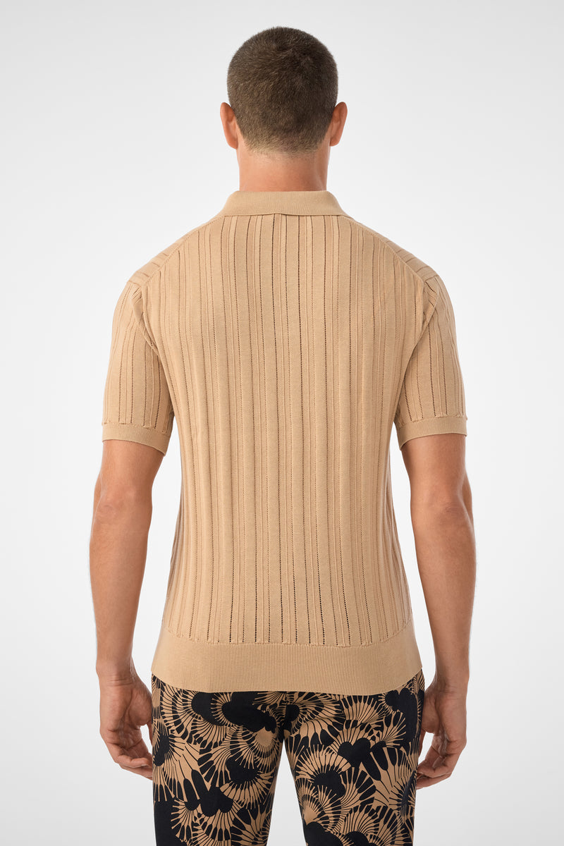 A man stands with his back to the camera, wearing the Kensington Short-Sleeve Polo in beige and navy pants with tan botanical patterns, set against a plain light background.