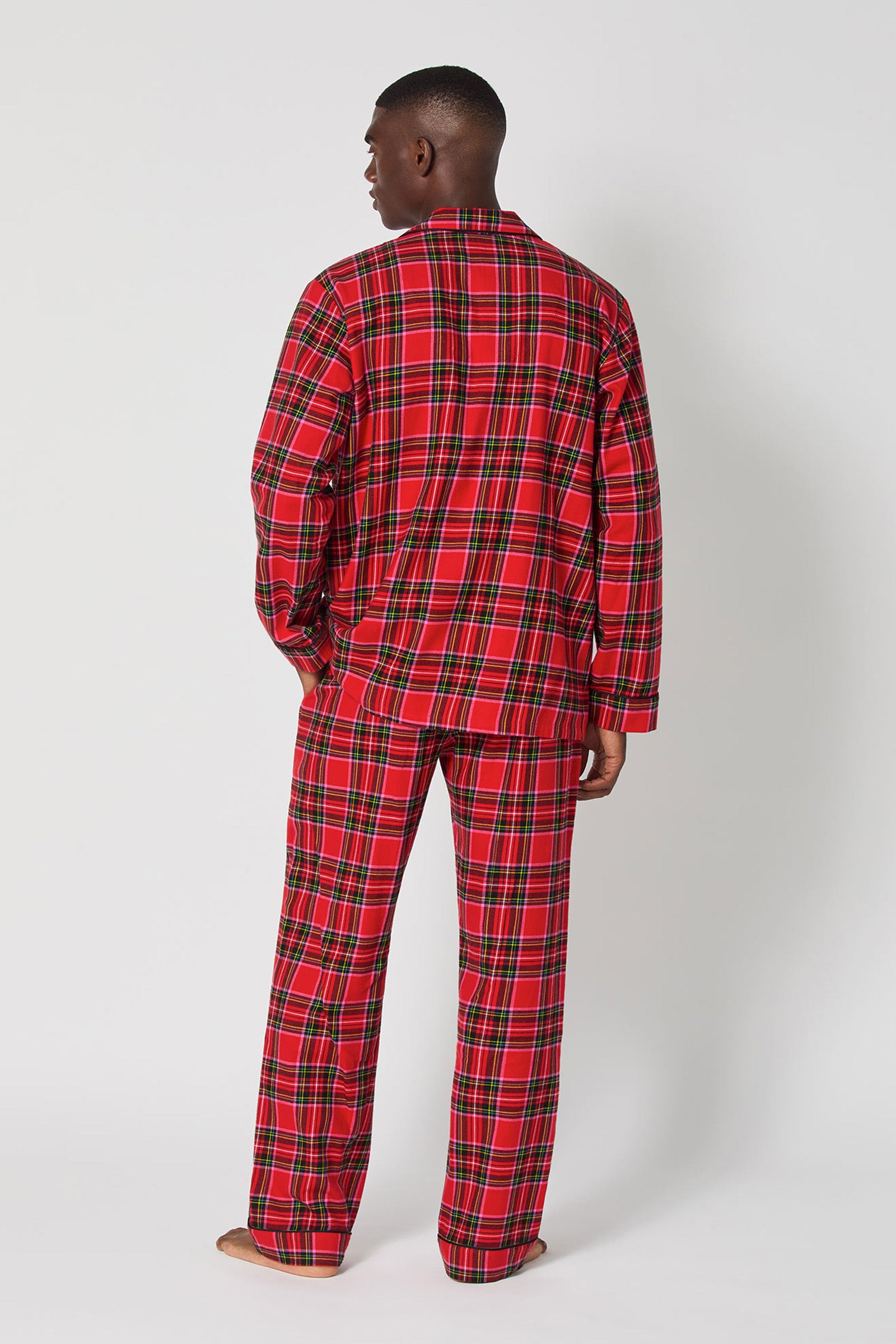 A man stands with his back turned, wearing the Christmas Plaid Men Classic Pj set featuring a red plaid long-sleeved shirt and matching pants against a plain white background.