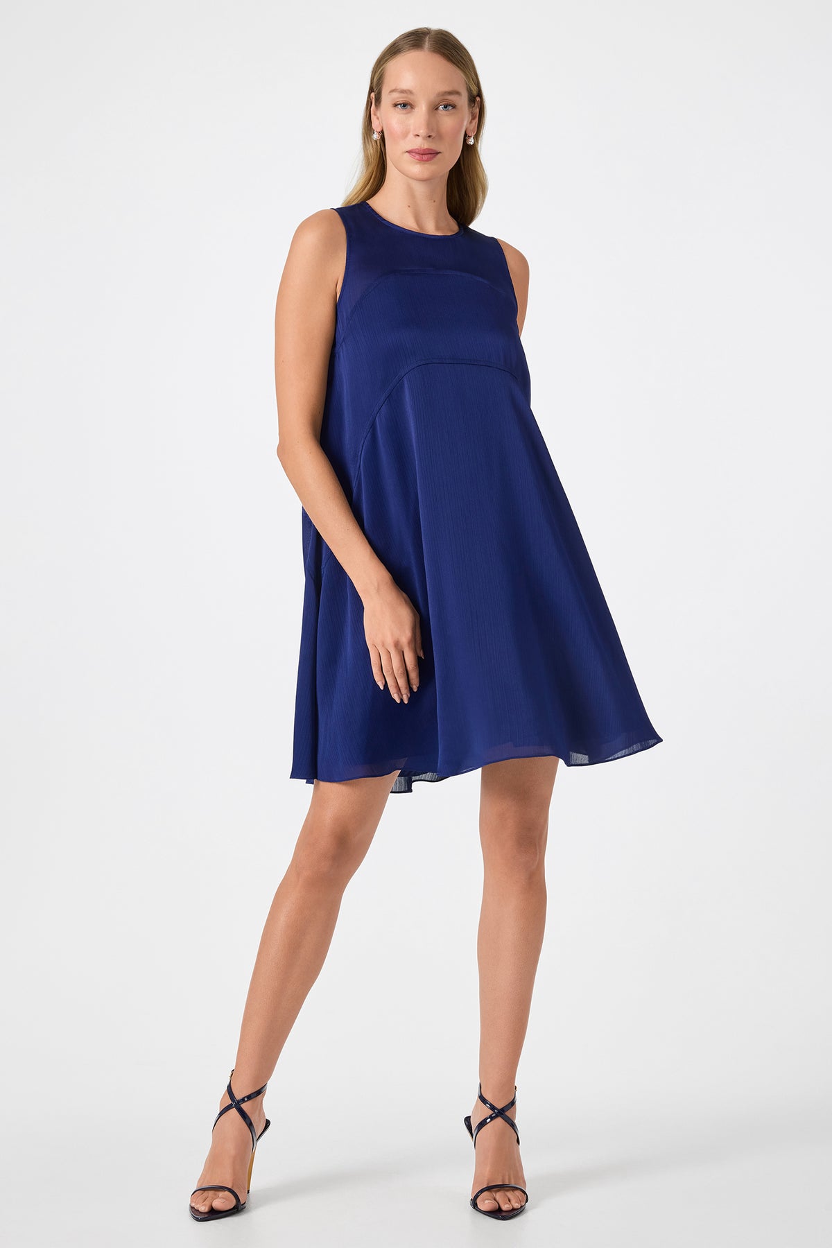A woman wearing the Mauvie Sleeveless Mini Dress and black strappy heels stands against a plain white background, looking confidently at the camera.