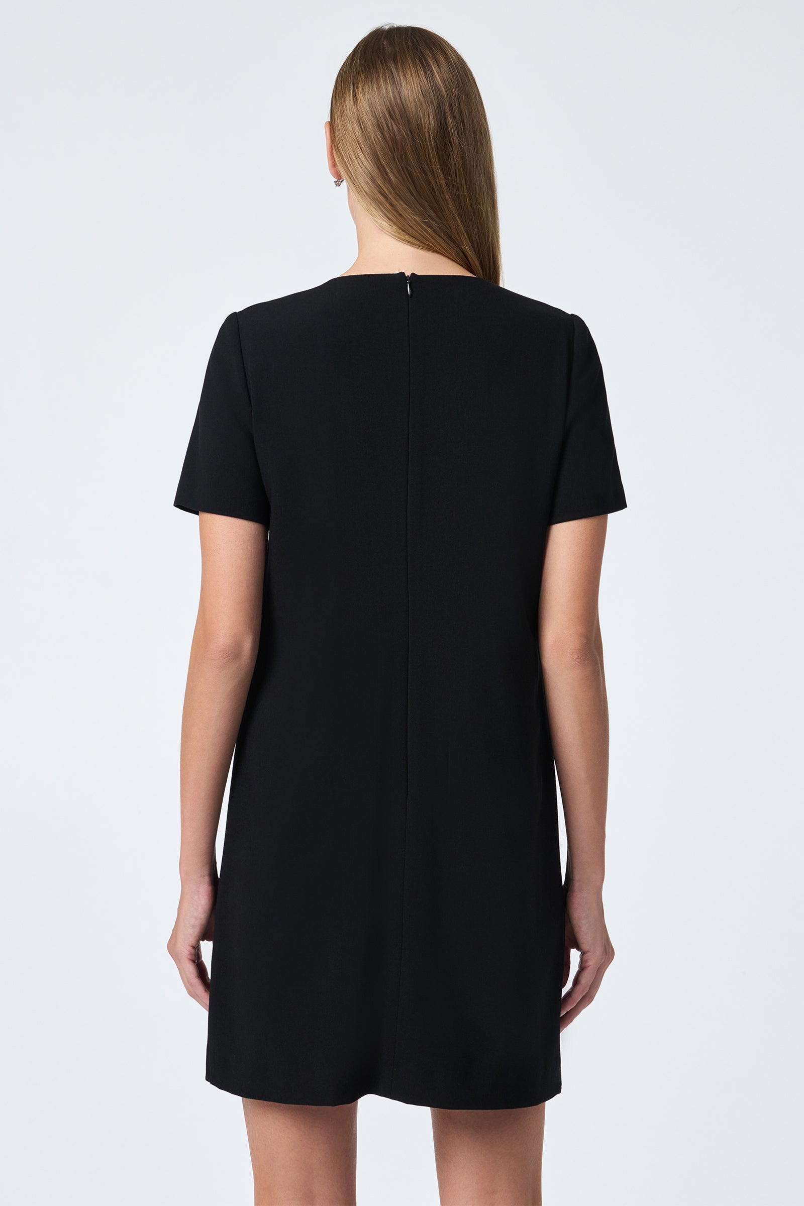 A woman with straight, light brown hair stands facing away, wearing the Diamonds Crystal Bows Sheath Dress—short-sleeved and knee-length—against a plain light background.