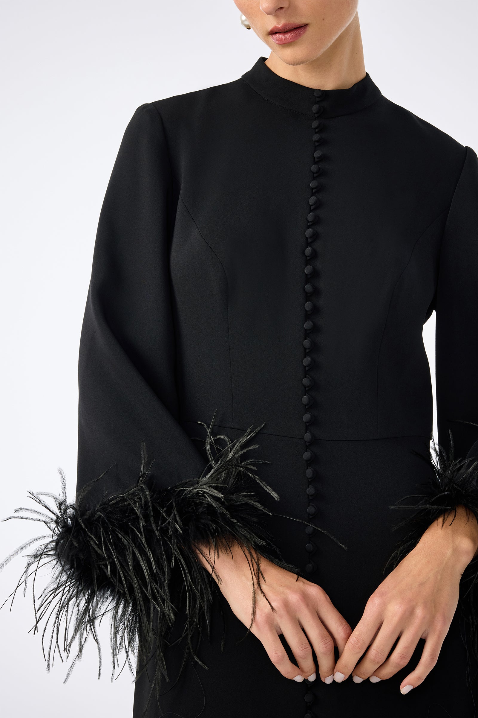 A woman wears the Montmarte Dress—a black, long-sleeve dress with front buttons and feathered cuffs—shown from shoulders to waist against a plain background.