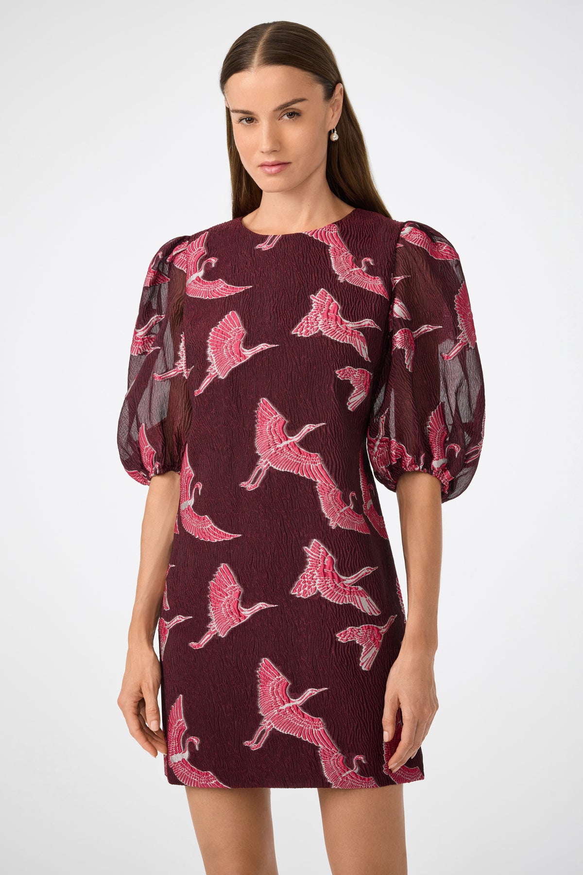 A woman wearing the Ringo Short Puff Sleeve Mini Dress, featuring a maroon color with pink bird patterns and sheer voluminous three-quarter sleeves, stands against a plain light background.