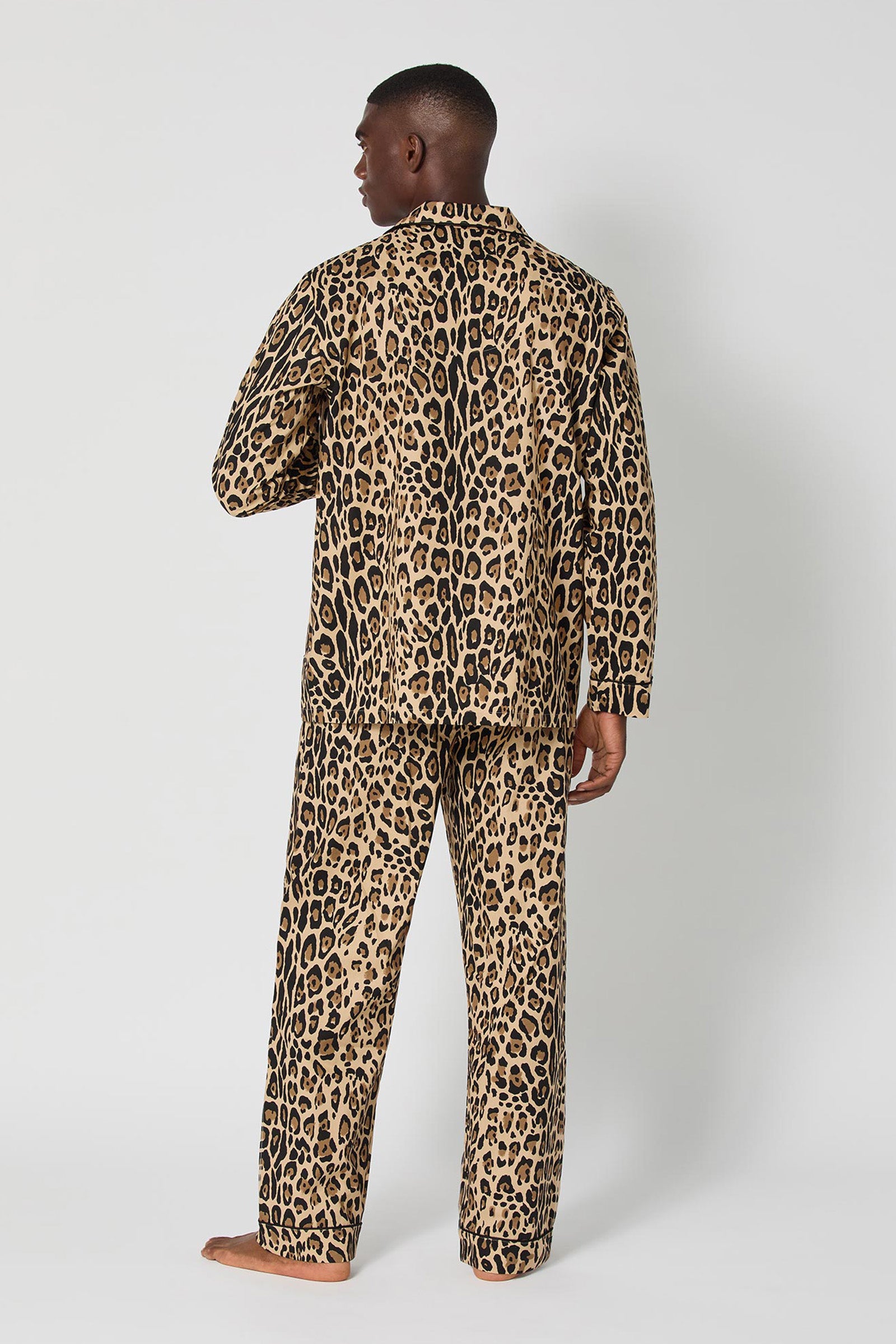 A man stands barefoot facing away, wearing the Leopard Stripe Mens Classic Pj set with a bold leopard print pattern, against a plain white background.