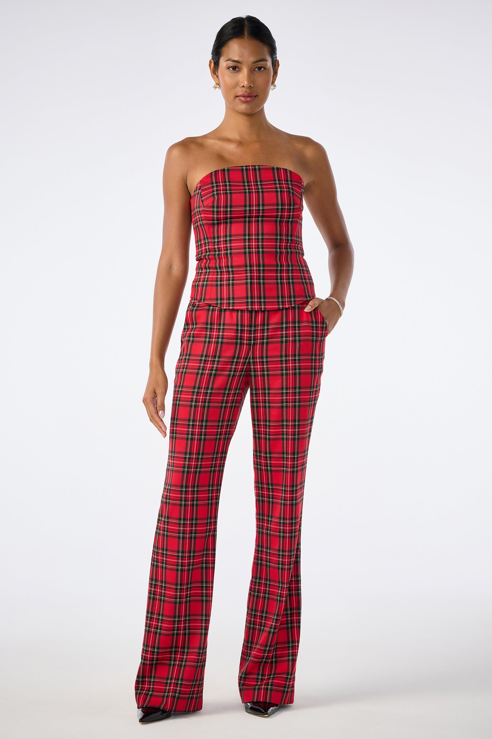 A woman stands against a plain background wearing the Arden Top, a strapless, fitted red plaid top, paired with matching high-waisted, wide-leg plaid trousers.