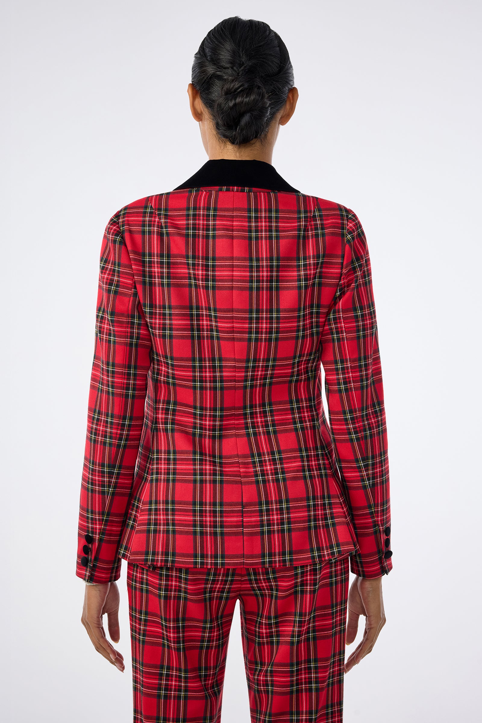 A person stands with their back to the camera, wearing the Revolution Jacket—a red plaid suit featuring black, white, and yellow stripes. Their hair is neatly tied back against a plain light gray background.
