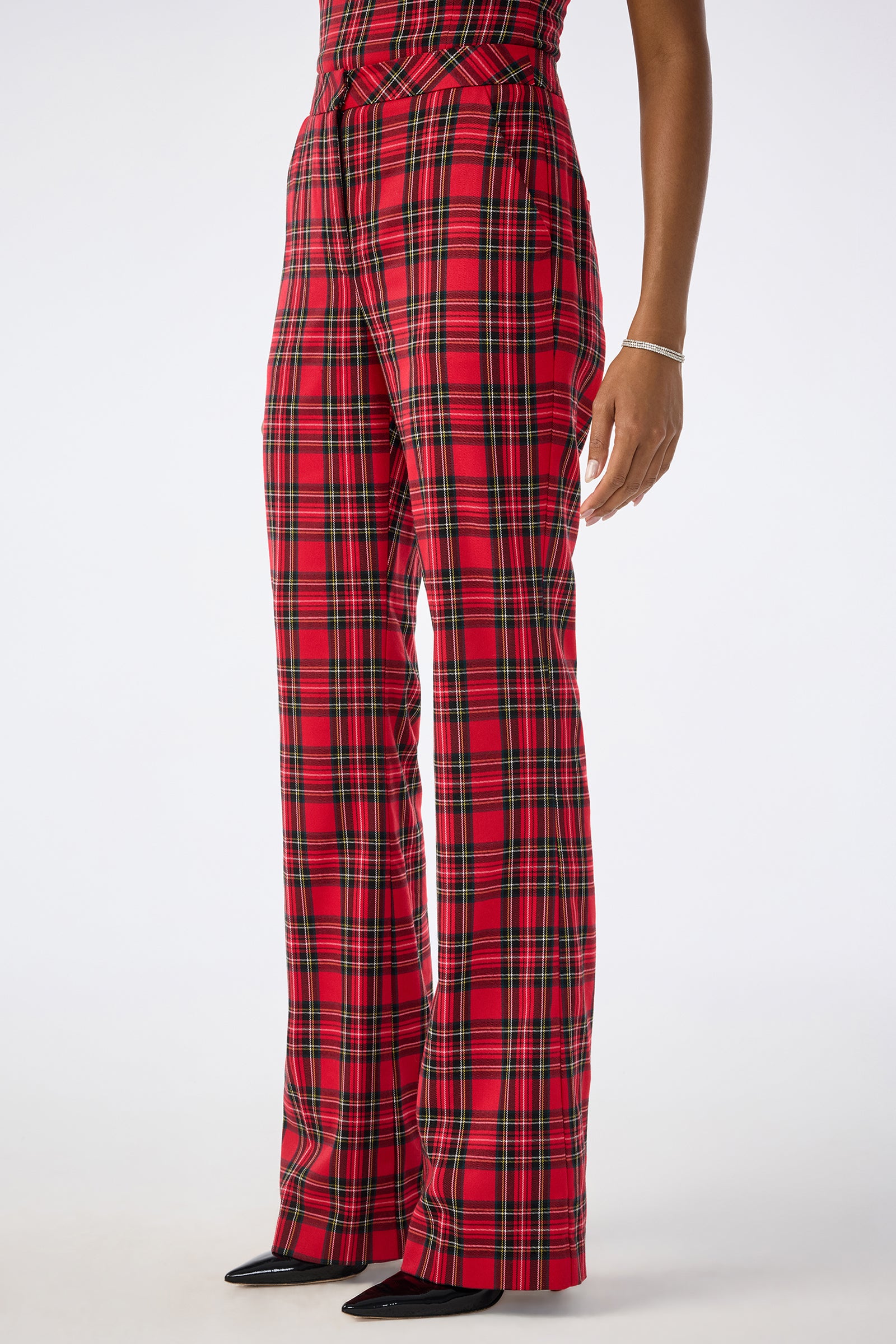 A person wears the Gorecki Pant—red plaid, high-waisted, wide-leg—with black pointed-toe shoes and a silver bracelet. Only one arm is visible; the upper body is mostly out of frame. The background is plain white.