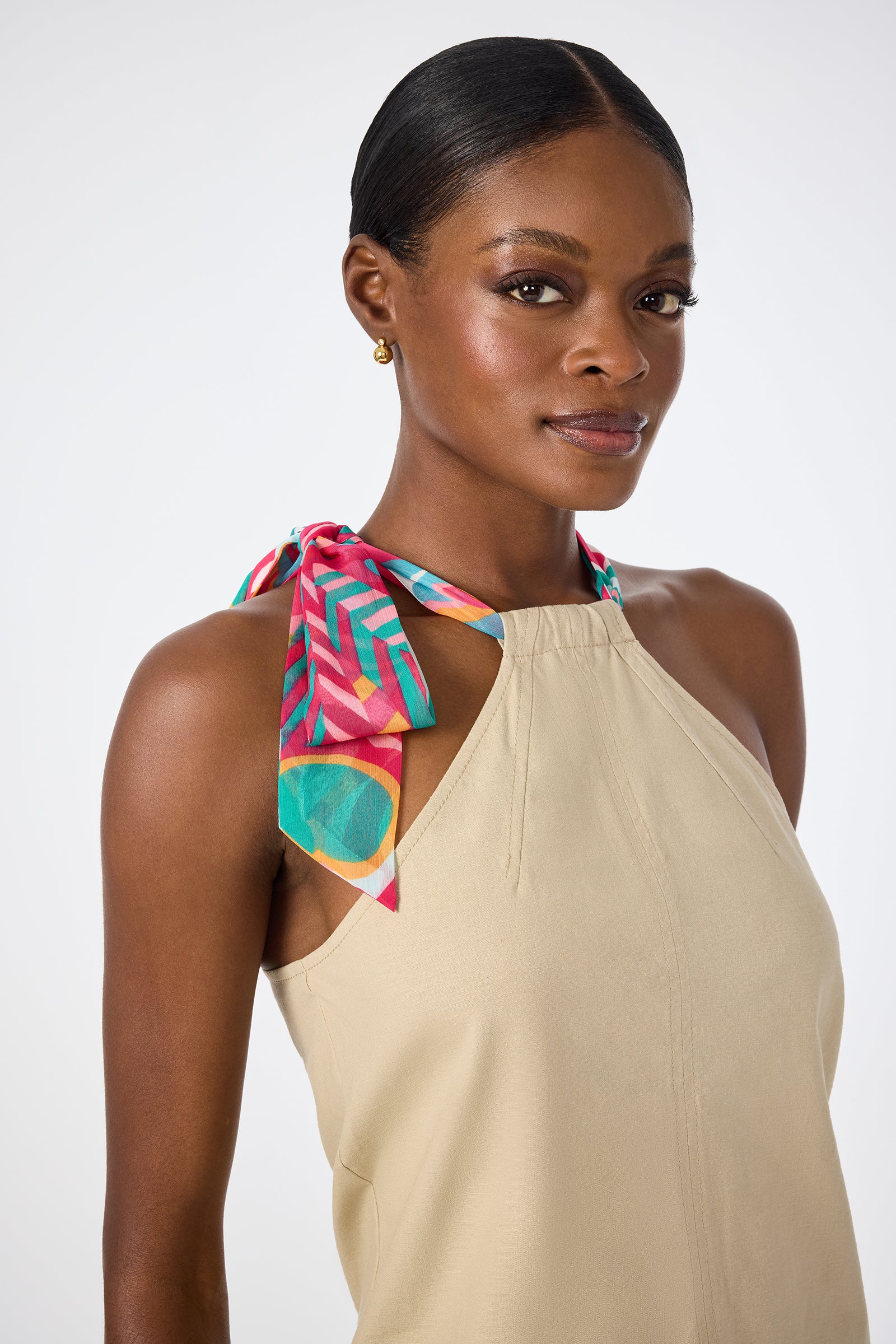 A woman confidently looks at the camera, wearing the Chatone Scarf Tie Halter Top paired with gold stud earrings and her hair neatly pulled back.