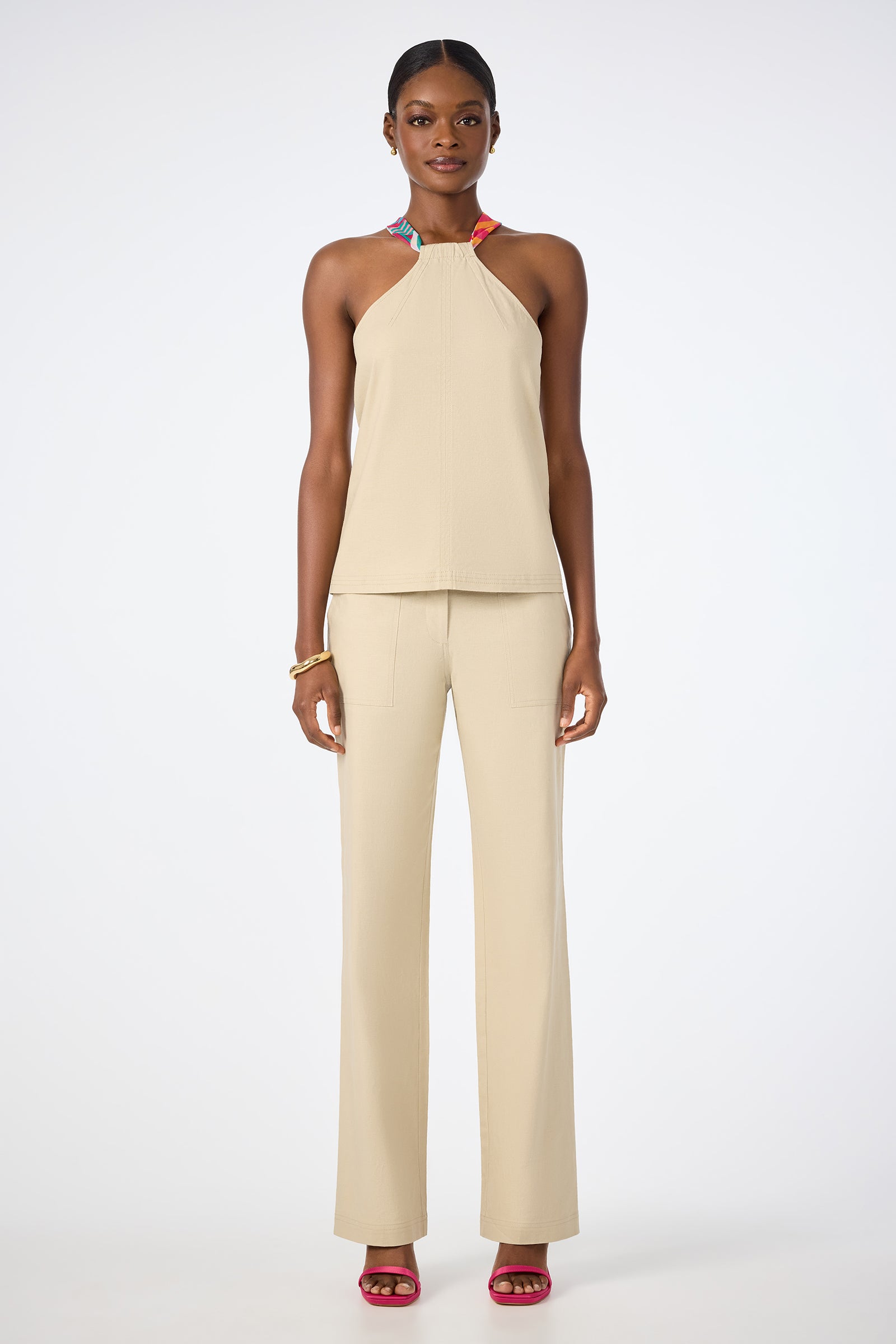 A woman faces forward wearing the beige Chatone Scarf Tie Halter Top with matching wide-leg pants, pink open-toe heels, hoop earrings, and a gold bracelet against a plain white background.