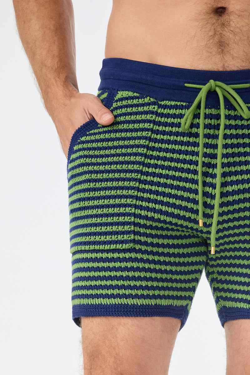 A person is wearing the August Knit Short in blue and green stripes with a green drawstring, posing with one hand in the pocket against a plain background.