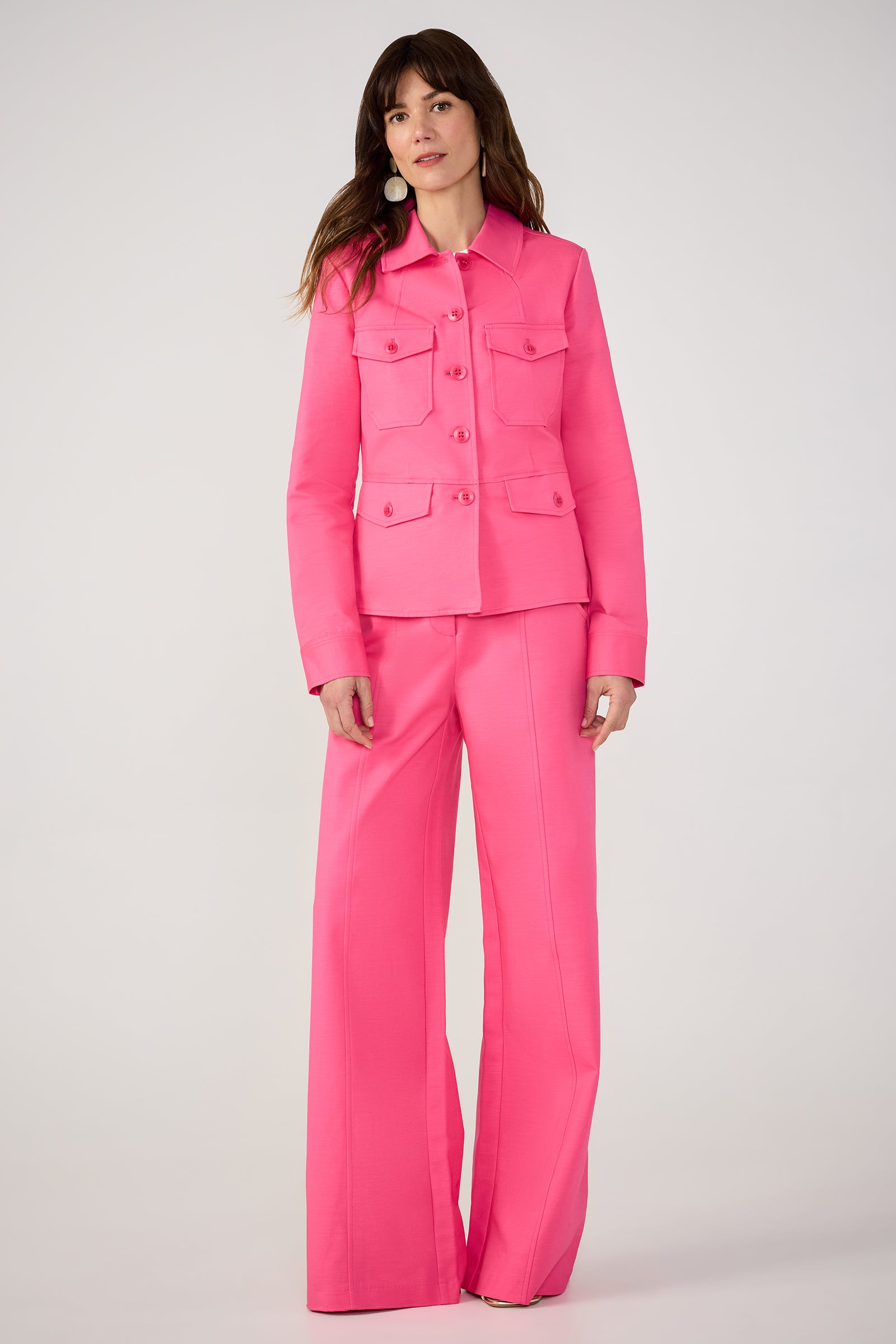 A woman stands against a plain background wearing the Half Court Wide-Leg Pant - Solid Suiting, featuring tailored wide-leg trousers and a buttoned jacket with flap pockets in bright pink.