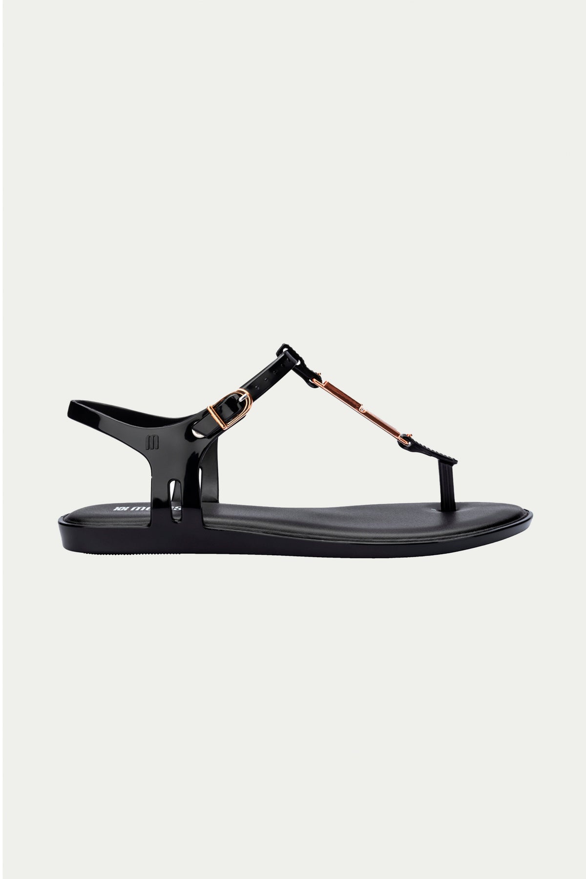 The Melissa Solar Chic T-Strap Sandal in black features a thong design, ankle strap with metallic gold buckle, and metal accents, shown against a plain light background.
