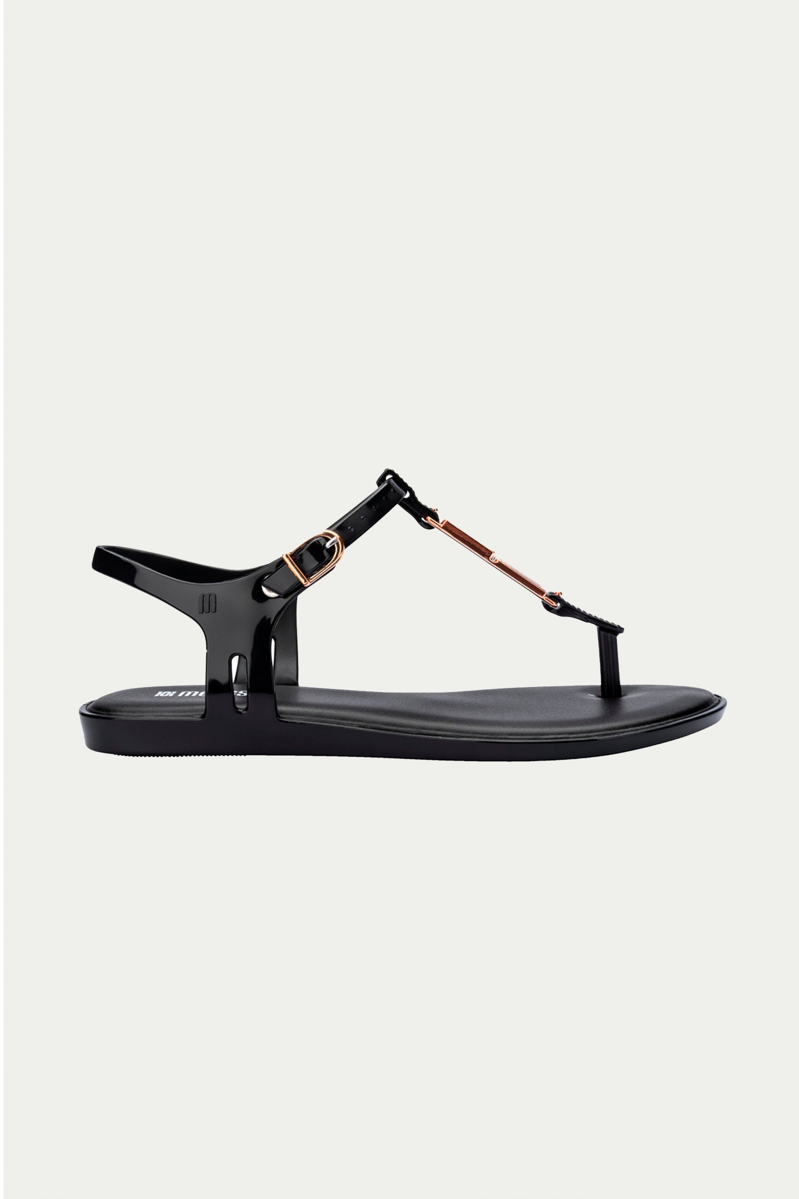 The Melissa Solar Chic T-Strap Sandal in black features a thong design, ankle strap with metallic gold buckle, and metal accents, shown against a plain light background.