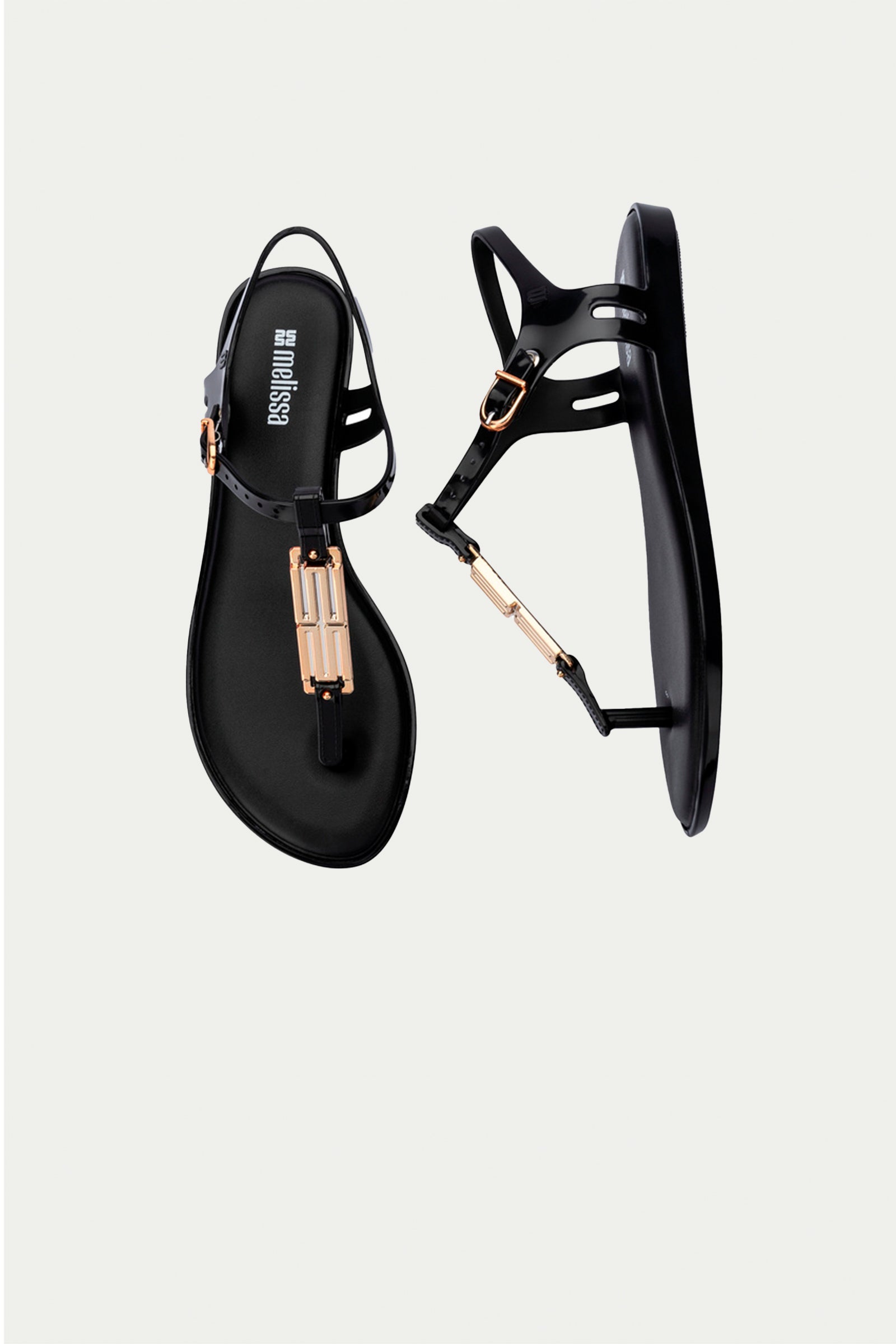 The Melissa Solar Chic T-Strap Sandal in black features a thong design, gold metallic accents on the straps, and a buckle closure.