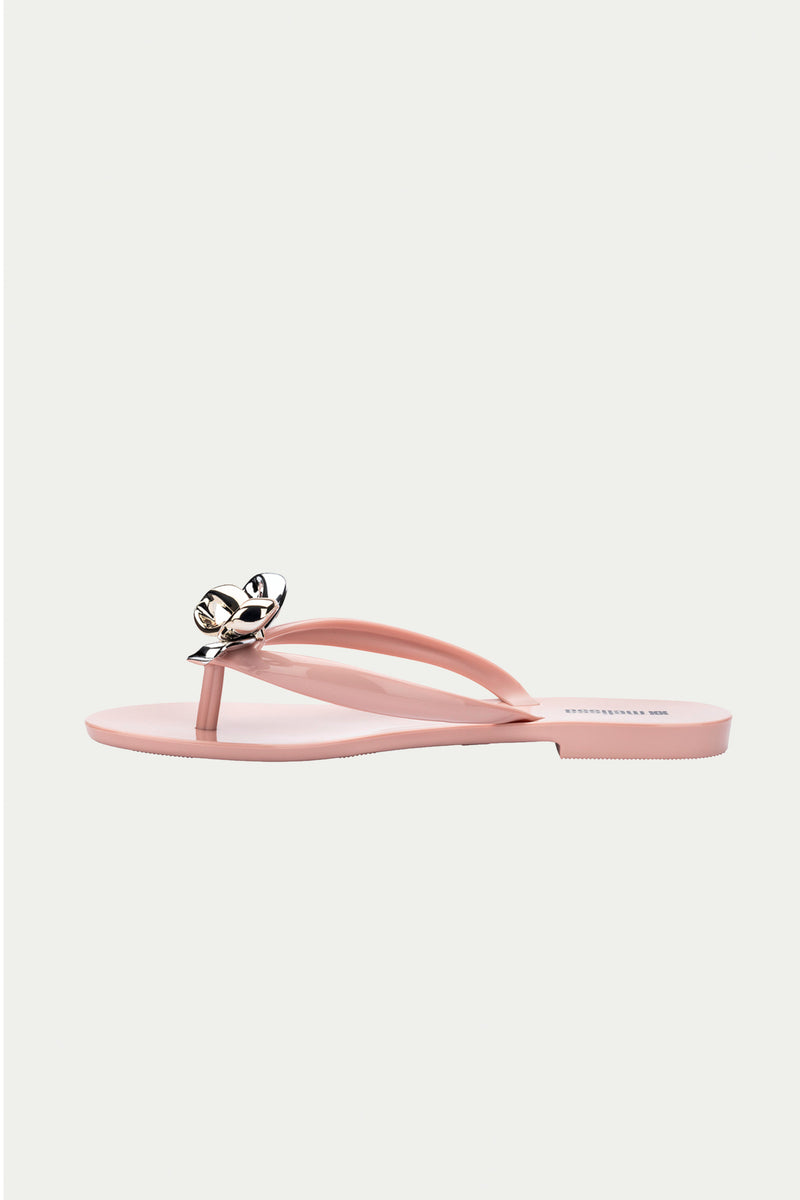 The Melissa Harmonic Eclipse Bow Sandal in pink features a thong strap with a metallic silver floral accent, shown against a plain light background.