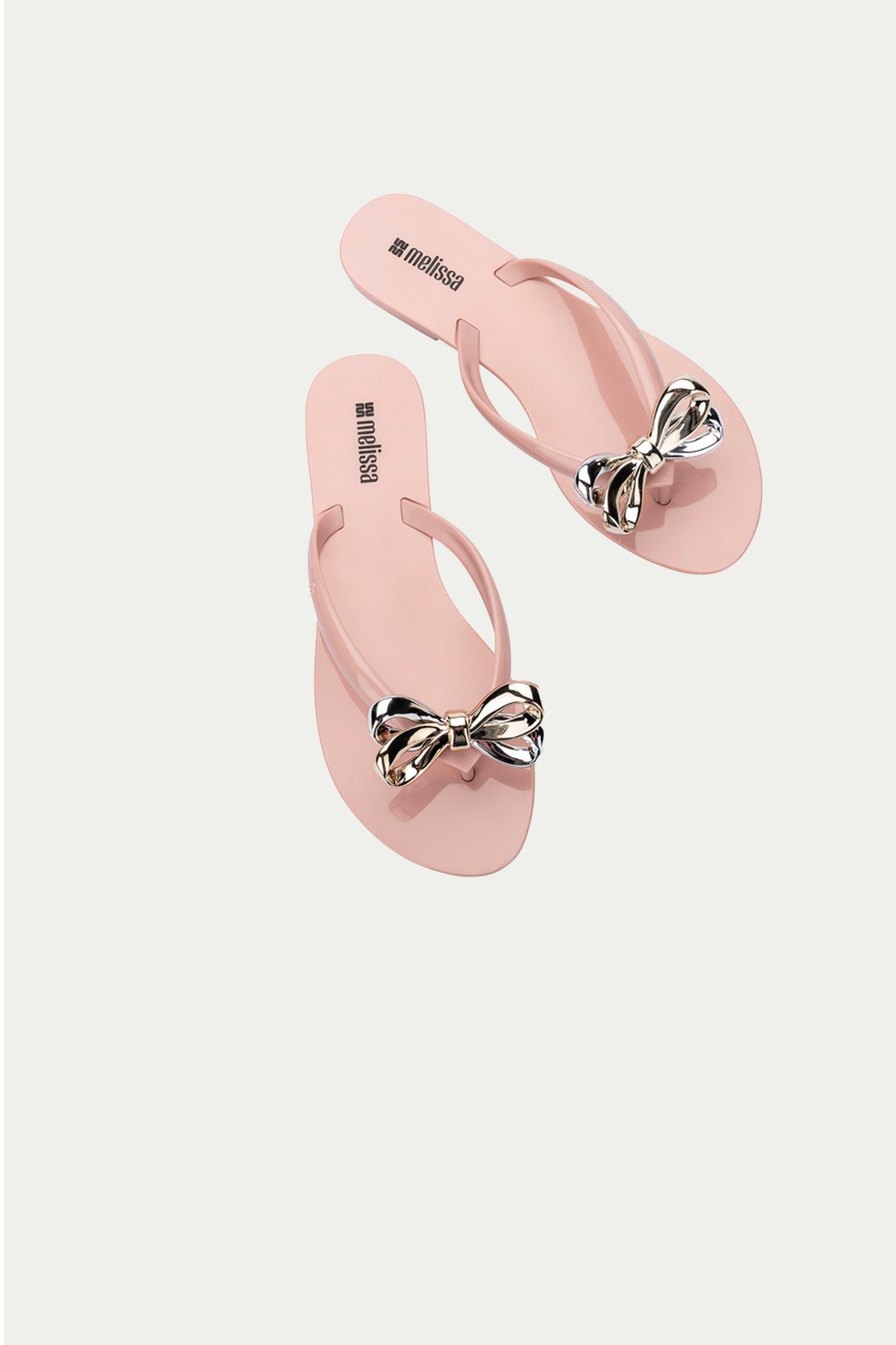 The Melissa Harmonic Eclipse Bow Sandal in light pink features metallic bows on the straps and is displayed against a plain white background.