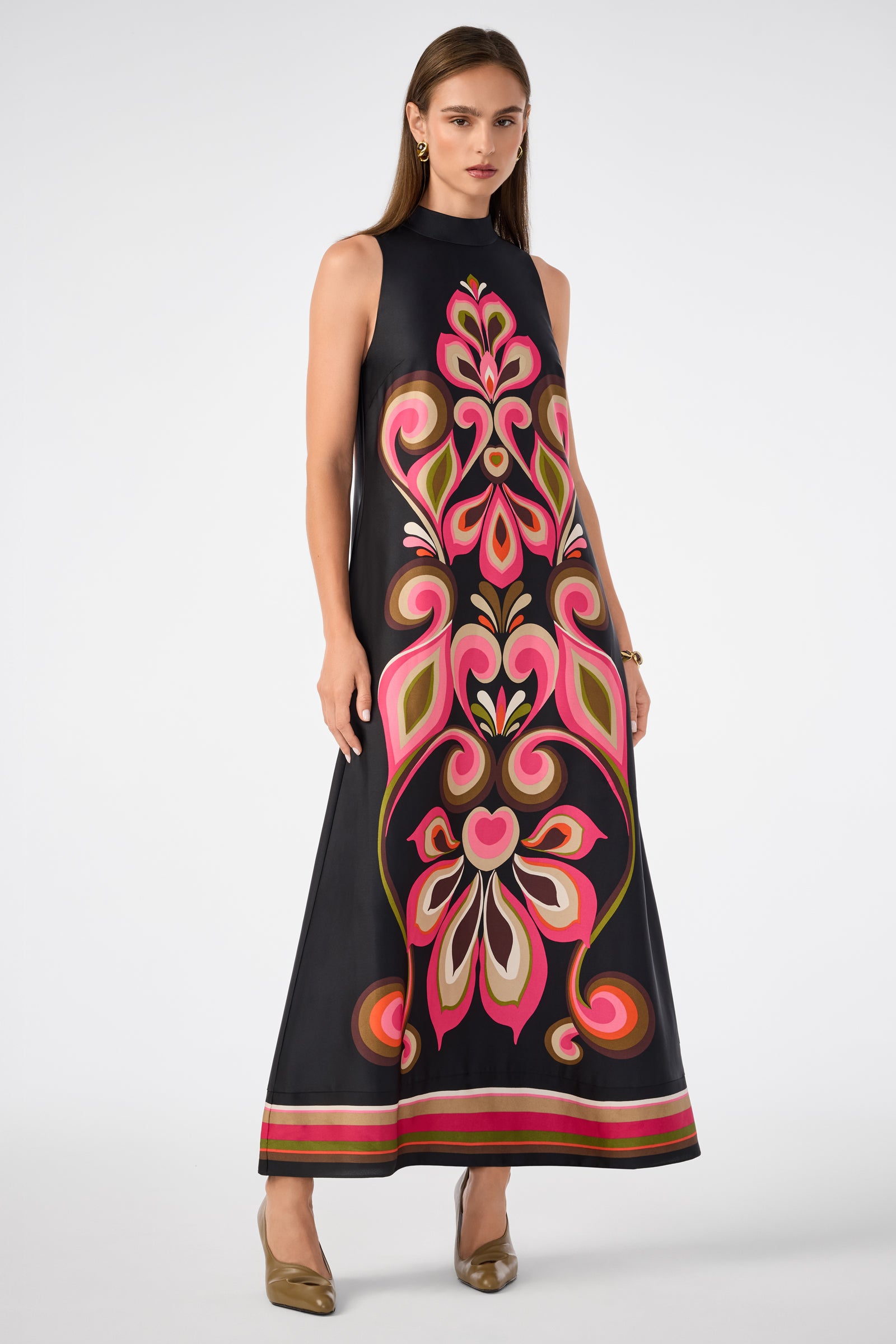 A woman stands against a white background wearing the Loveage Sleeveless Maxi Dress in Sanctuary, featuring bold pink, red, and green floral patterns on black, paired with brown shoes.