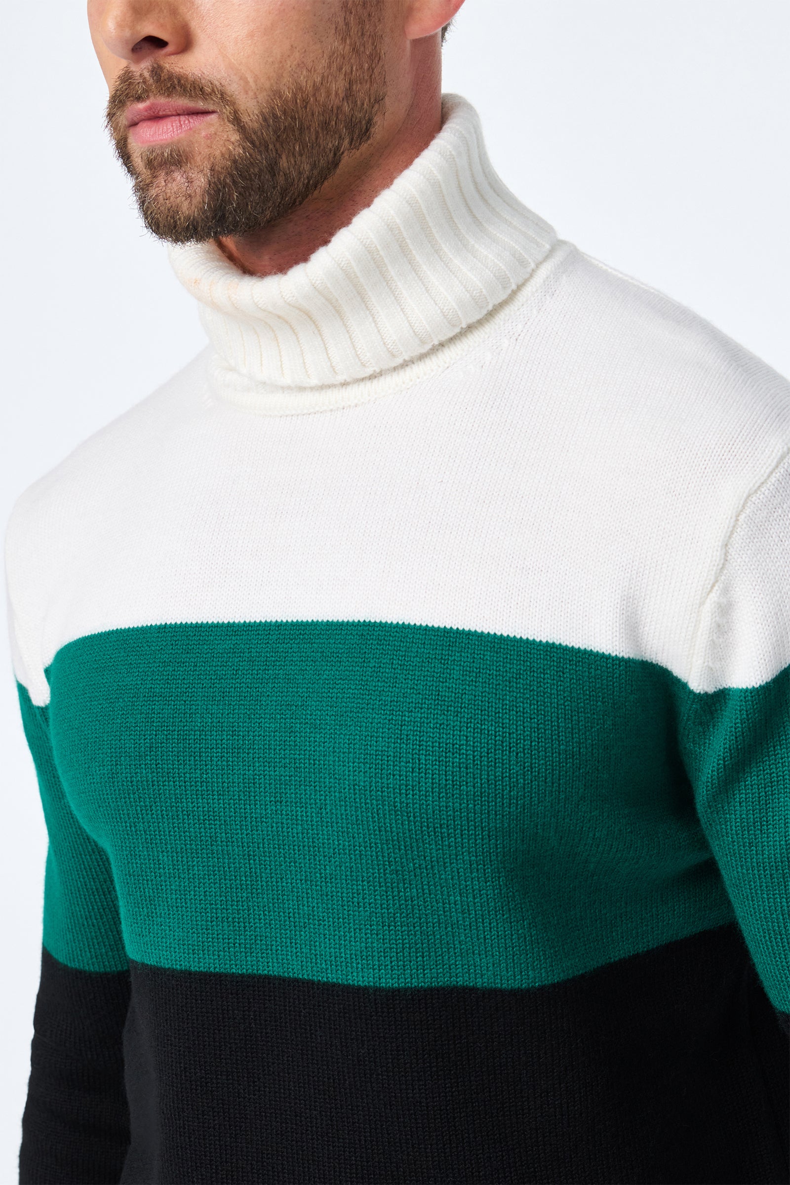 A man models the Harrelson T-Neck, a color-block turtleneck sweater featuring white on top, green in the middle, and black on the bottom, shown from the shoulders up against a plain background.