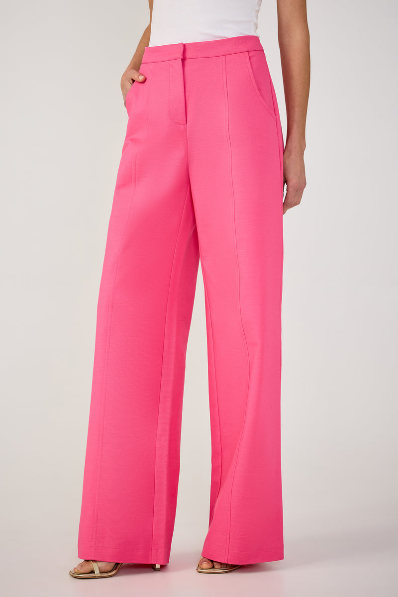 A person wears the Half Court Wide-Leg Pant - Solid Suiting in bright pink, paired with a white sleeveless top and open-toed heels, standing with one hand in a pocket against a plain light background.