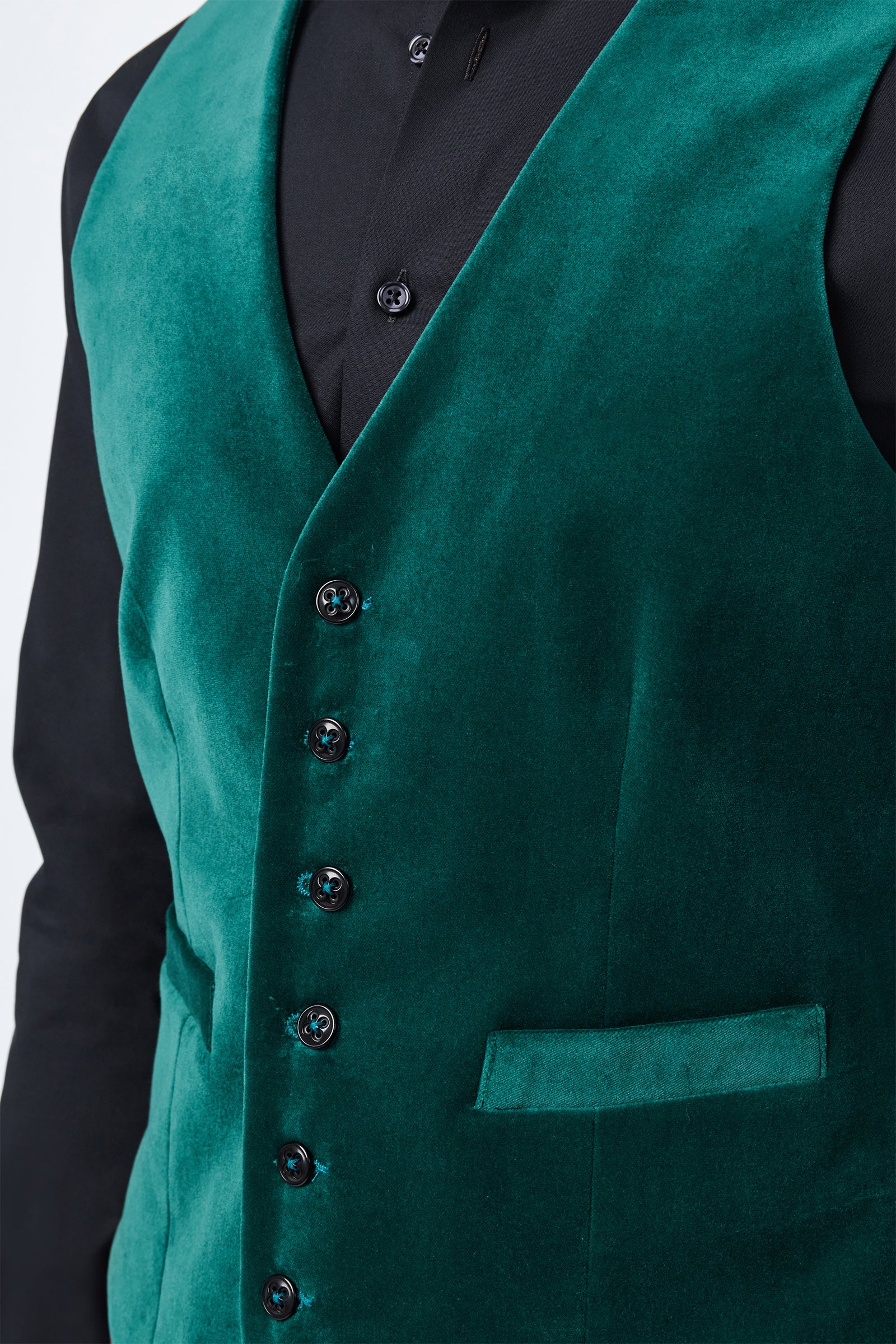 A close-up of a person wearing the Irving Vest in deep green velvet over a black dress shirt, featuring black buttons and a welt pocket.
