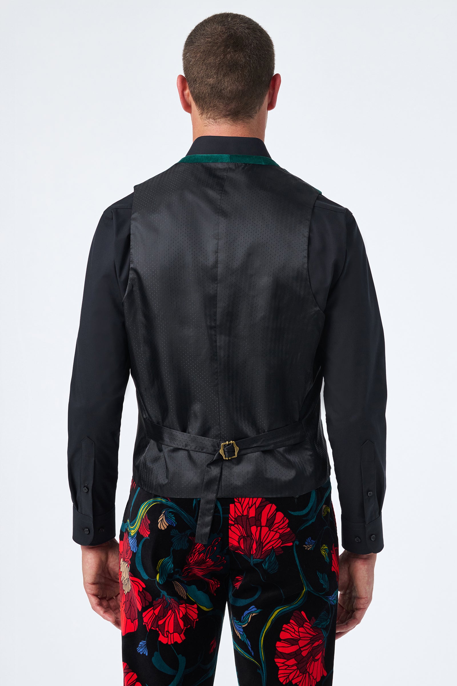 A man is seen from behind wearing a black dress shirt, the Irving Vest with a buckle at the back, and dark pants featuring a bold red floral pattern.