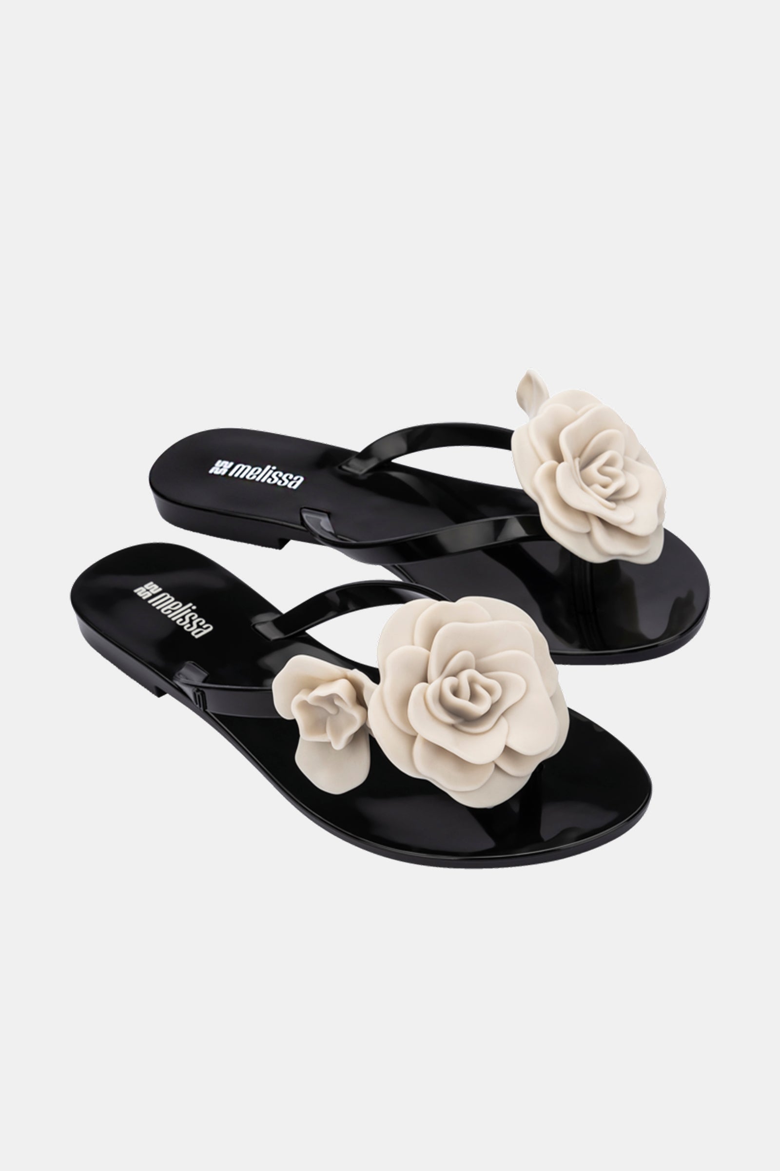 The Melissa Harmonic Petals Sandal is a glossy black thong sandal featuring large cream 3D flower accents on the straps, shown against a plain white background.