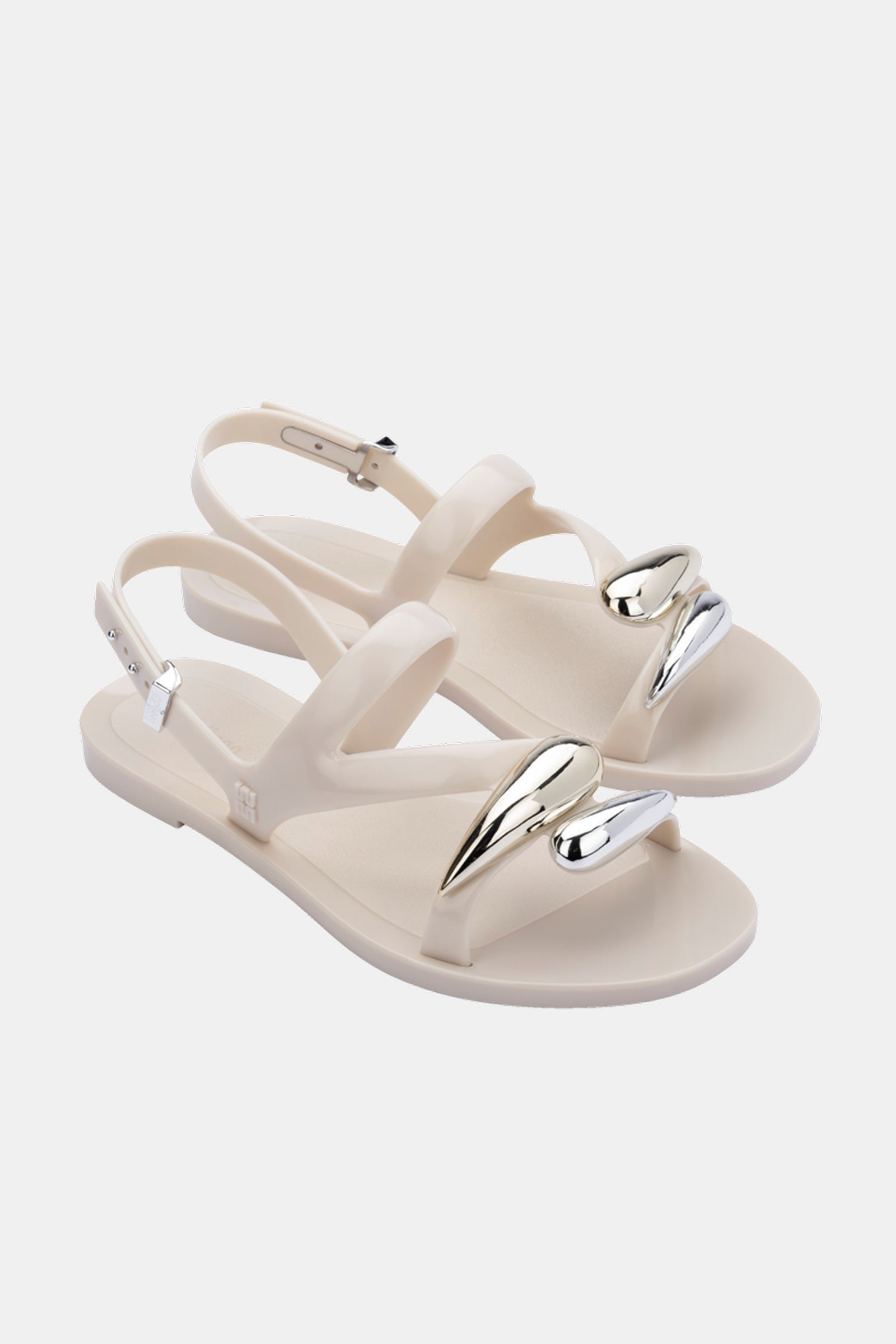 The Melissa Iris Sandal is a cream-colored open-toe sandal with ankle straps and metallic silver heart-shaped accents on the front straps, shown against a white background.