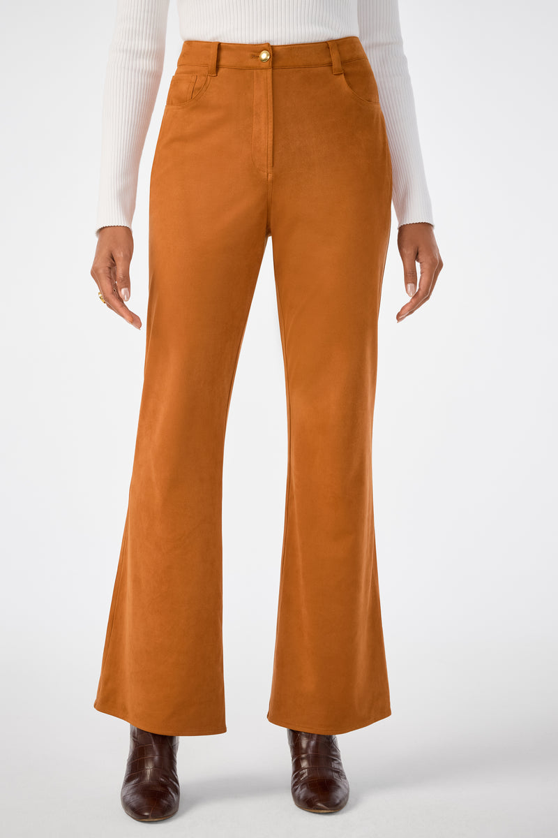 A person wearing the Apple Bottom Pant, high-waisted and rust-colored with a flared cut, paired with a white ribbed long-sleeve top and brown ankle boots, stands against a plain white background.