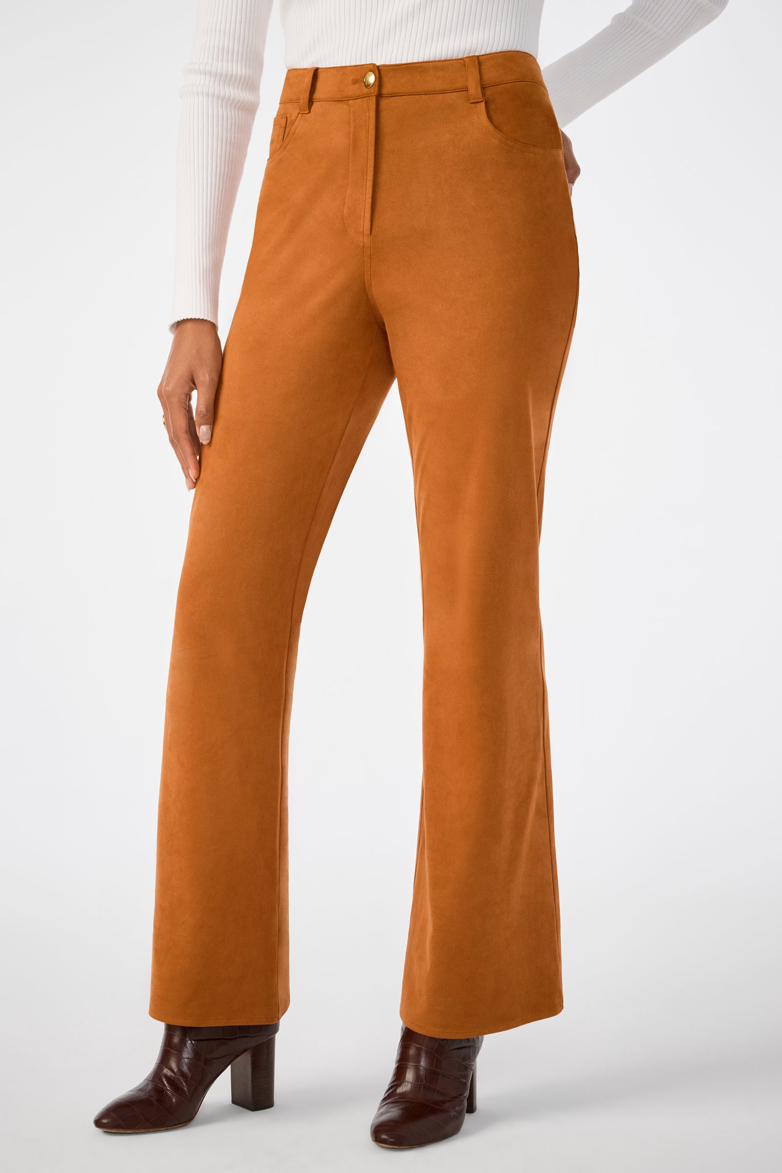 A person wearing the Apple Bottom Pant—high-waisted, burnt orange suede with flared legs and front pockets—paired with a white ribbed top and brown heeled ankle boots, stands against a plain white background.