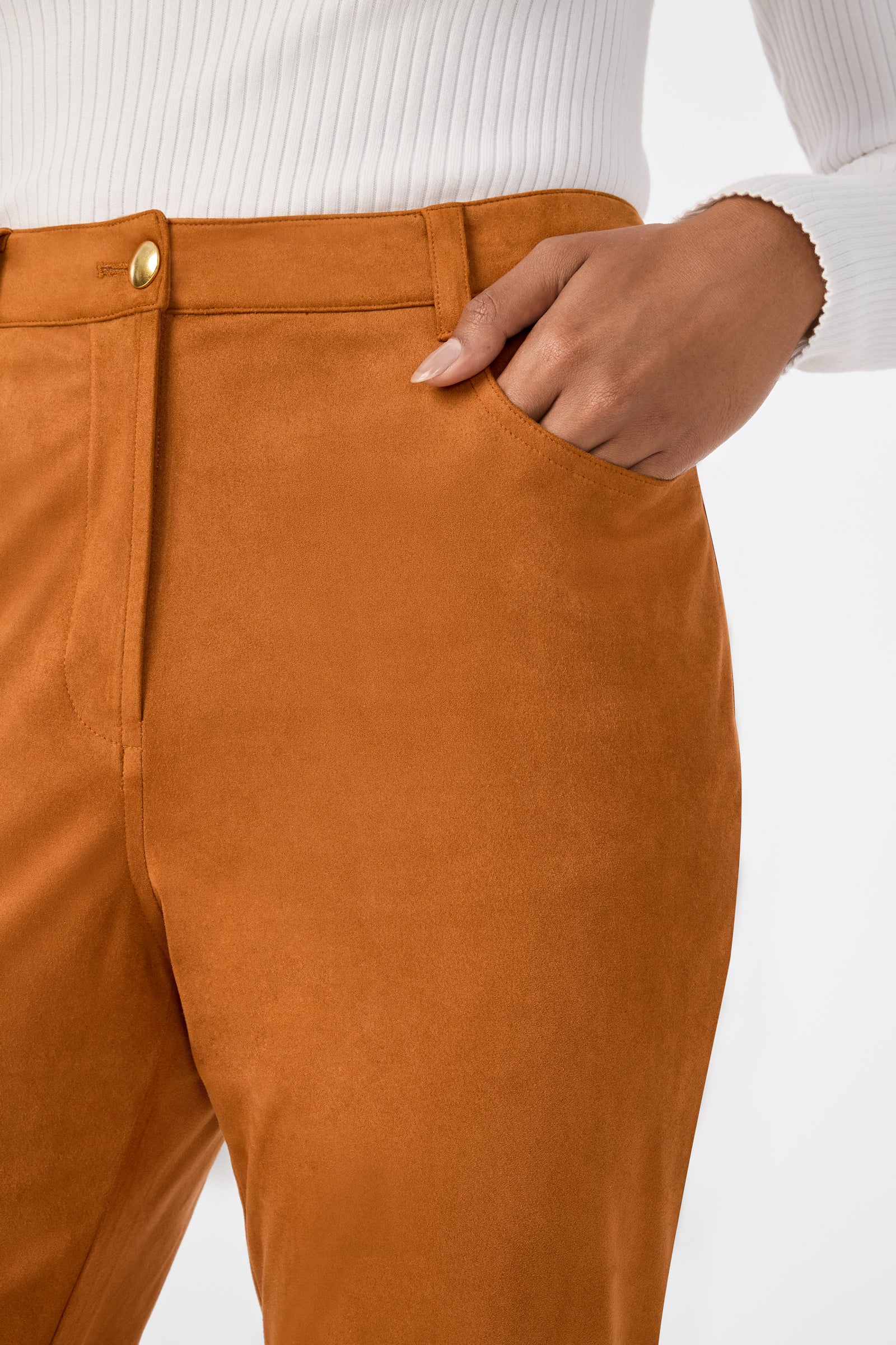 A person wearing Apple Bottom Pant, a high-waisted caramel suede style, paired with a white ribbed long-sleeve top and one hand in the pocket.