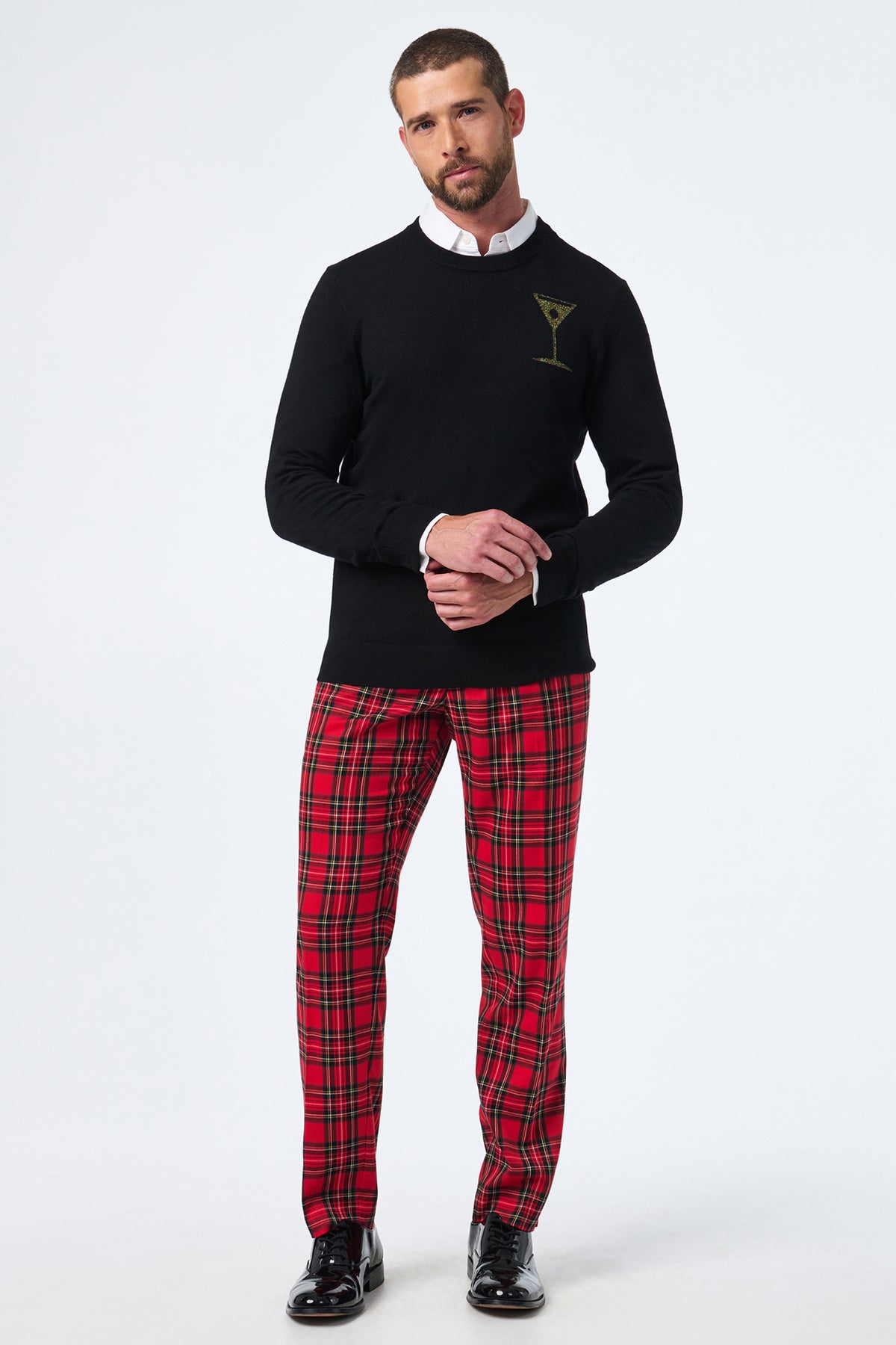 A man stands against a white background wearing the Martini Crewneck, red plaid pants, a white collared shirt, and black dress shoes. His hands are loosely clasped in front of him.