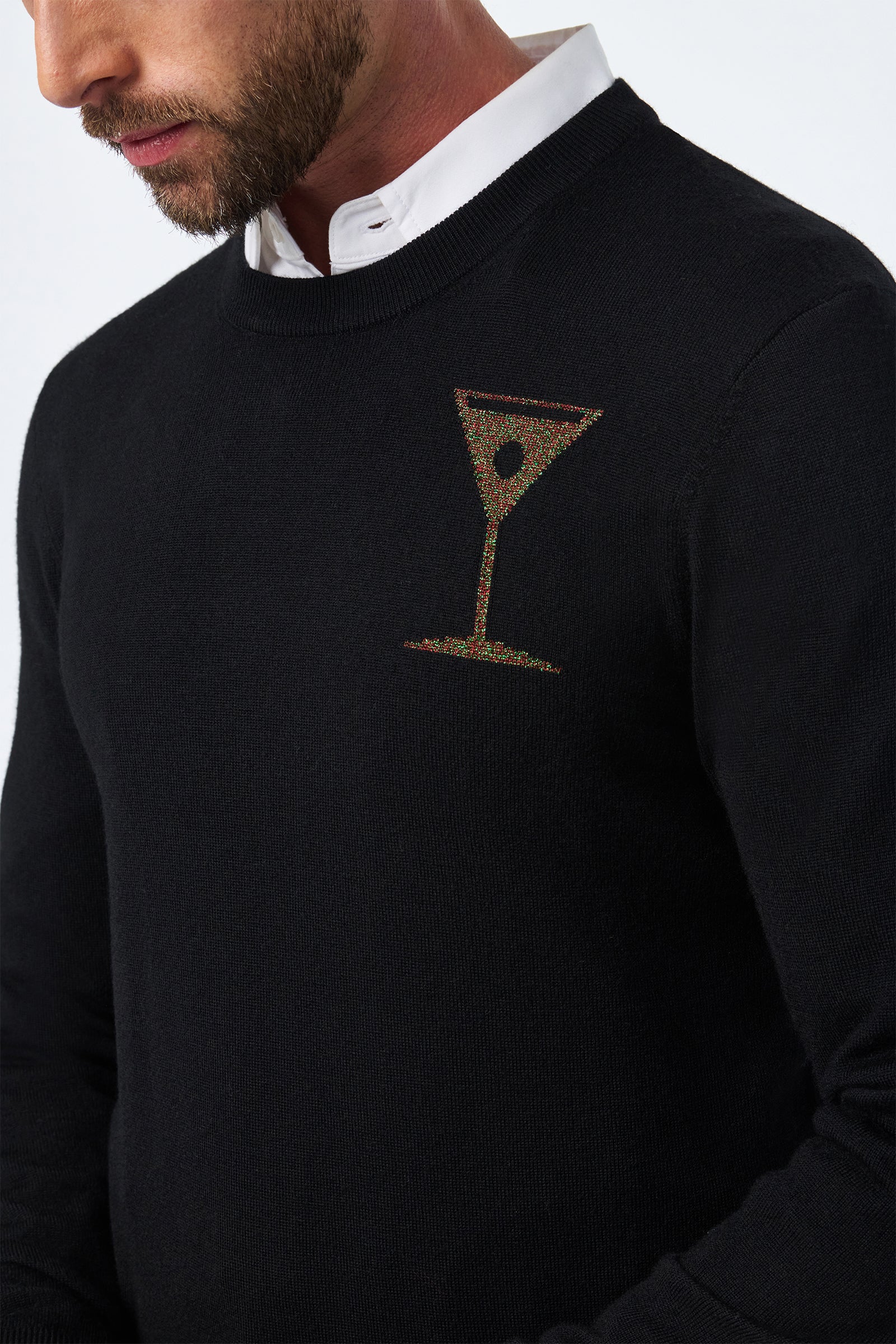 A man wears the Martini Crewneck—a black sweater with a small martini glass design on the chest—over a white collared shirt. The image is cropped to show only his lower face, neck, and upper torso.