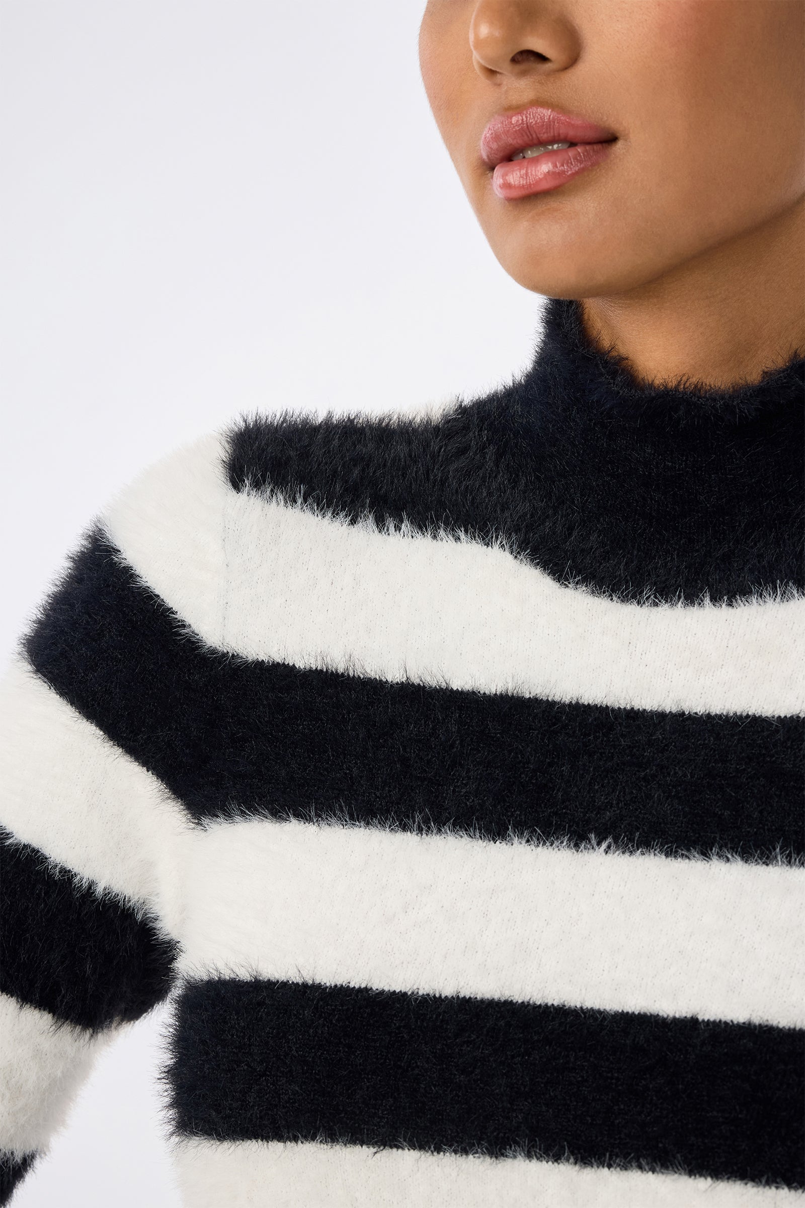 A person wears the Mali Mock Neck Sweater in fuzzy black and white stripes, shown from the shoulders up. Their face is partially visible with lips slightly parted.