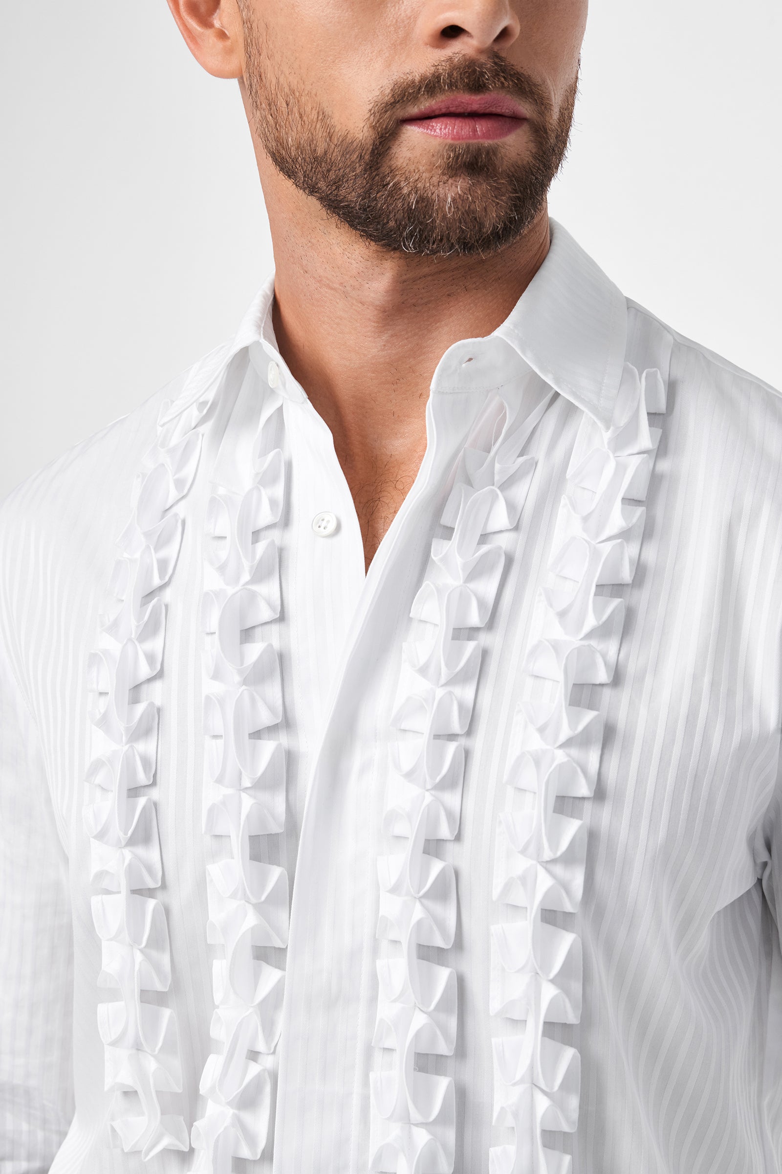 A man with a short beard wears the Evan Tux Shirt, a white dress shirt featuring vertical stripes and decorative ruffles down the front. The photo is cropped to partially show his face and upper torso.