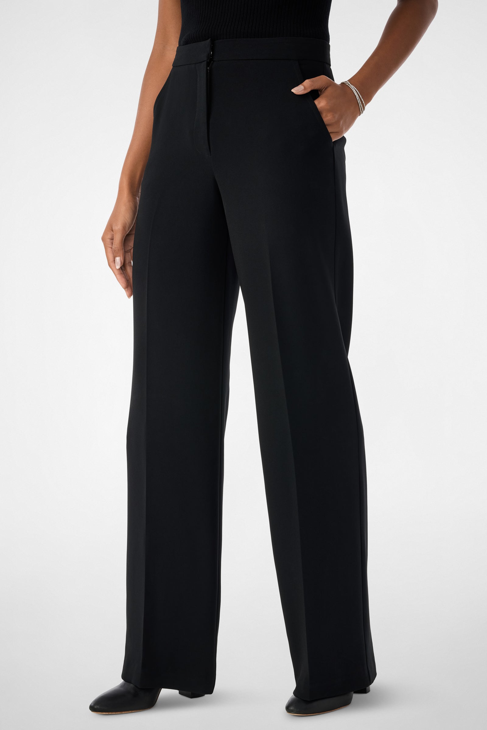 Wearing Sadie Wide-Leg Pants, a black sleeveless top, and black shoes, a person stands with one hand in their pocket against a plain light background.