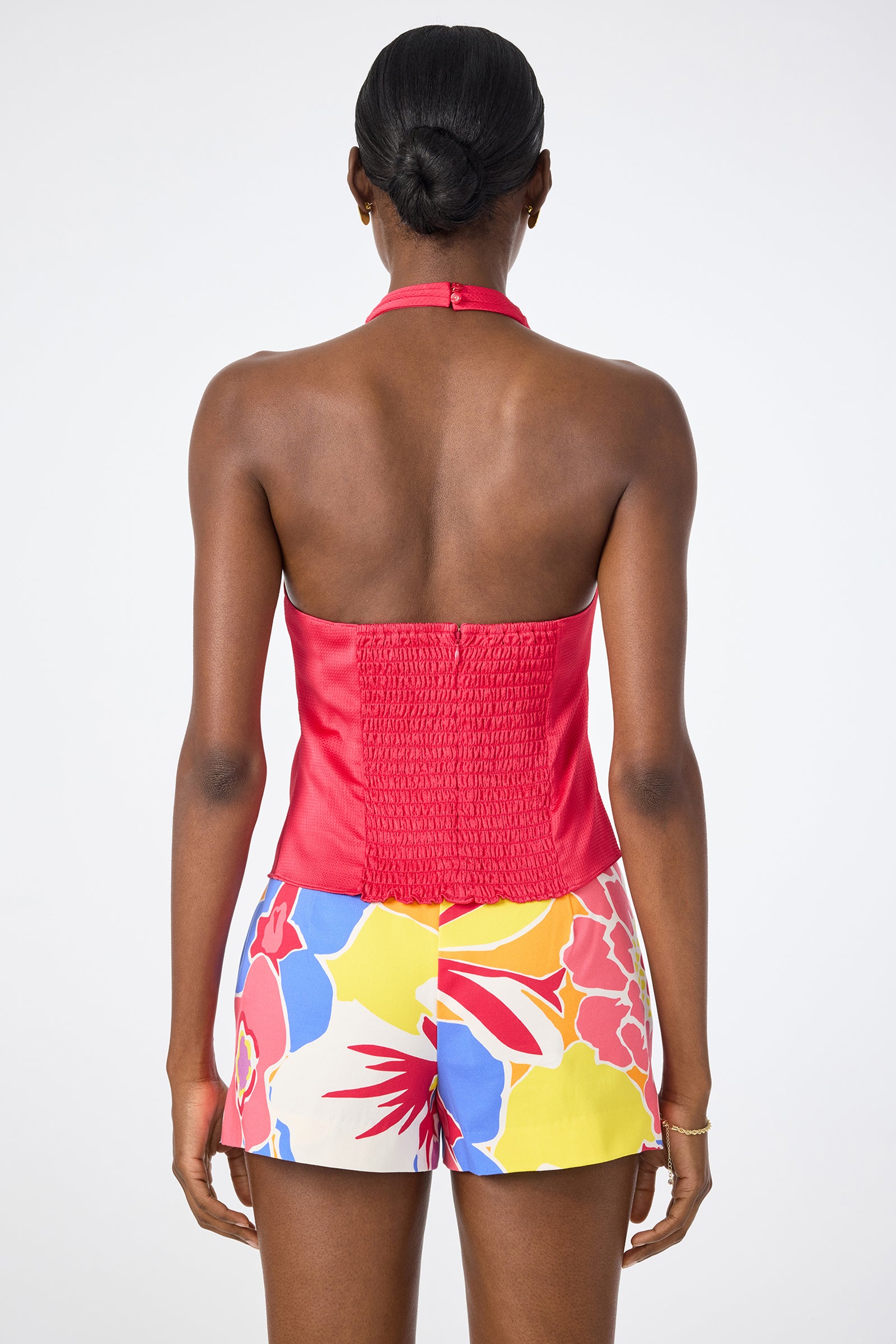 A person stands with their back to the camera, wearing the Lanika Halter Top in red and colorful floral shorts. Their hair is styled in a neat bun.