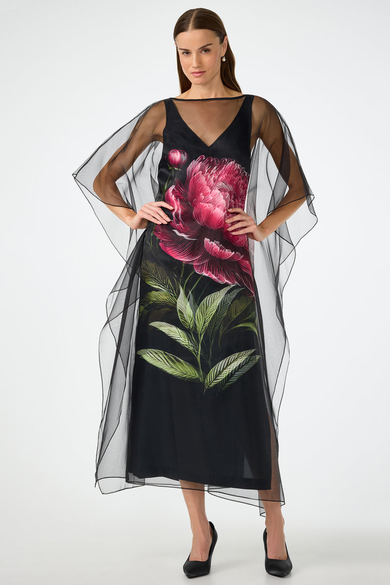 A woman poses with hands on hips in the Salon 2 Organza Midi Dress—a sheer black midi featuring wide, flowing sleeves and a bold pink flower with green leaves printed on the front. She completes the look with black heels.