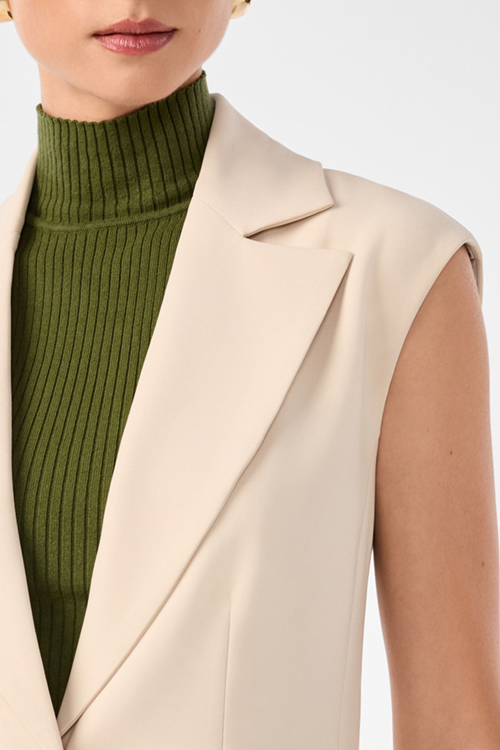 A person in the Boabab Sleeveless Jacket layered over a green ribbed turtleneck, with only the lower face and upper torso visible against a plain background.