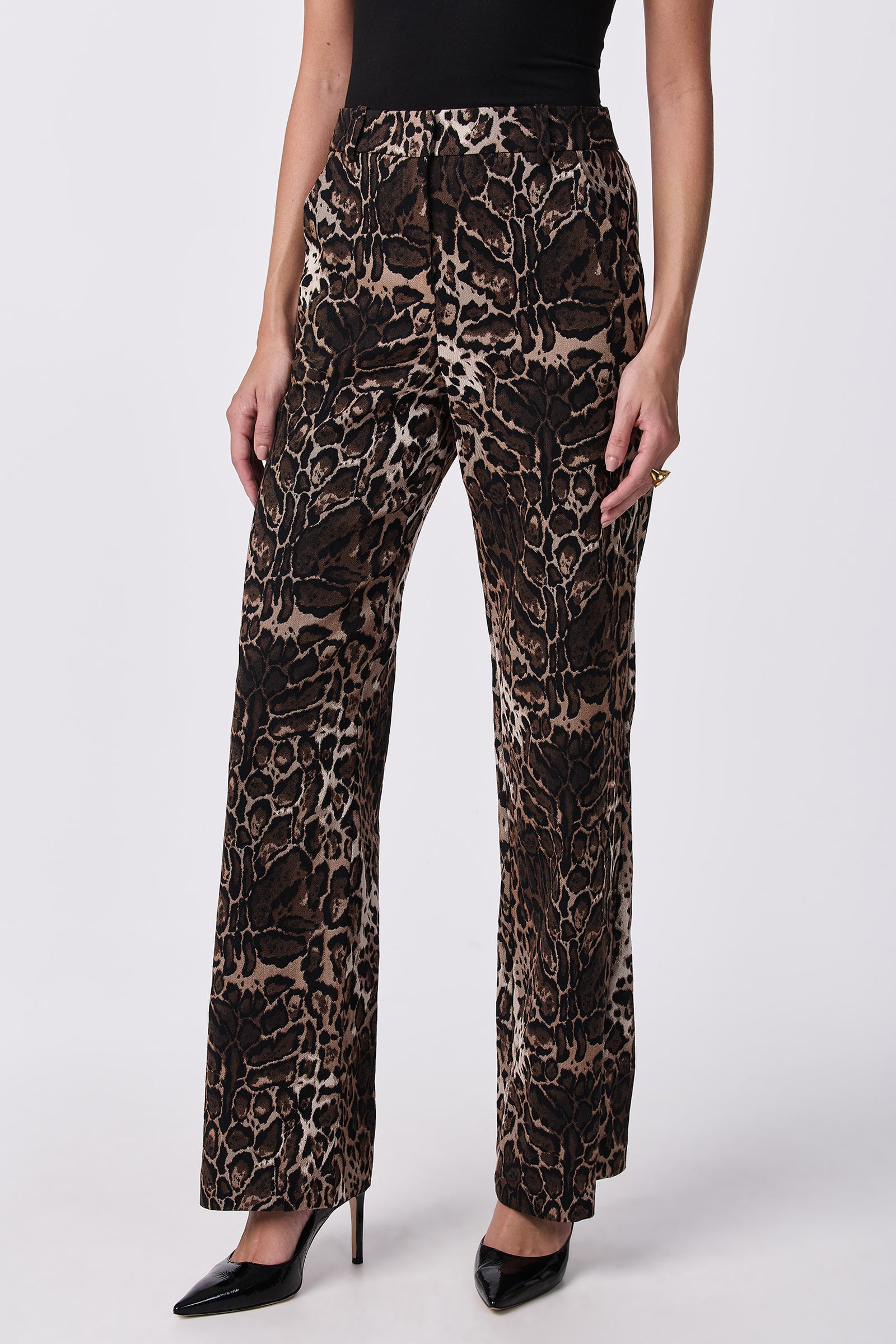 Model wears the Kendi Wide-Leg Pants in a bold brown and black animal print, paired with a black top and pointed-toe heels, posing against a plain white background.