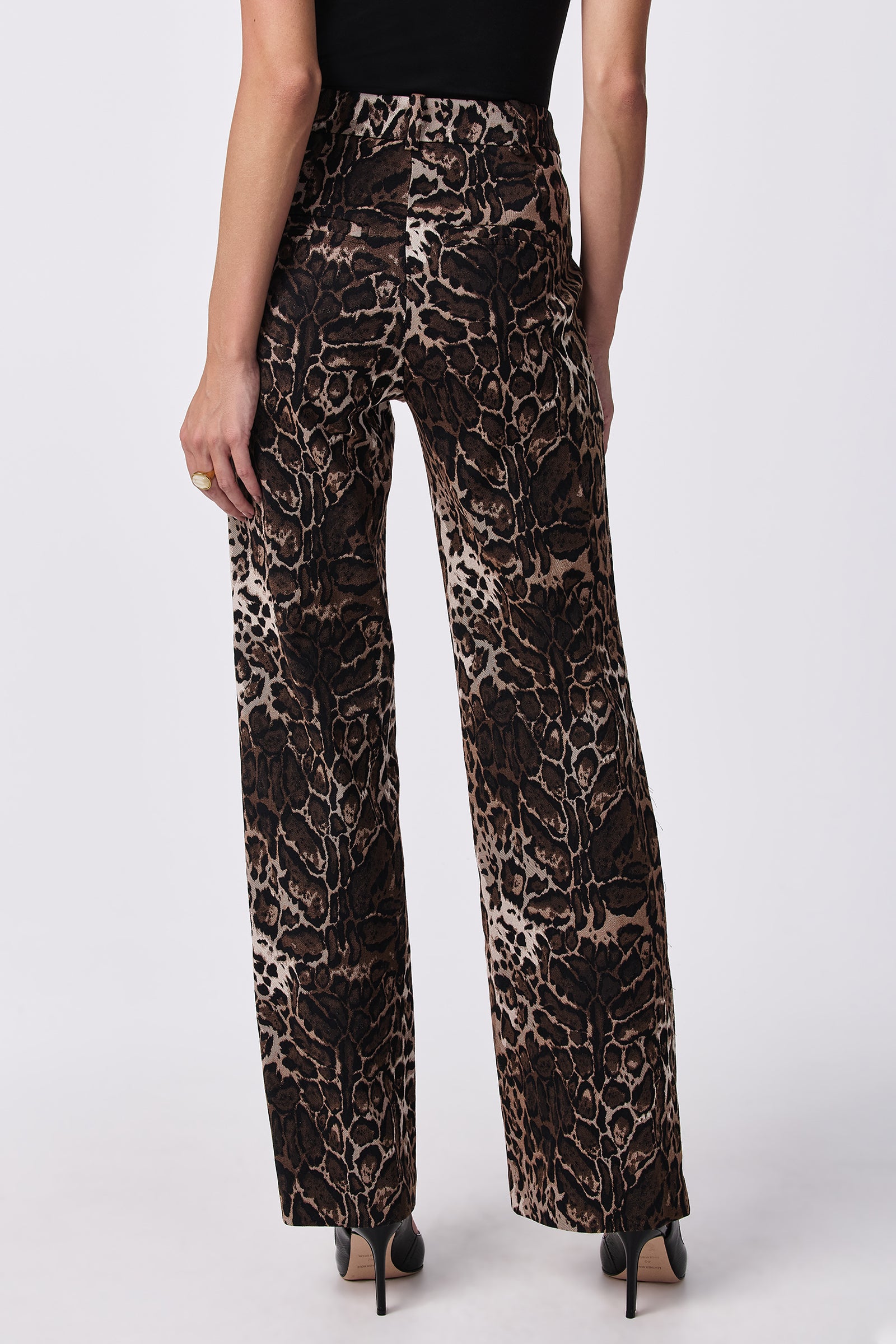 Model wears the Kendi Wed-Leg Pants, featuring a brown and black animal print, paired with a black top and black heels. Photographed from the back against a white background.