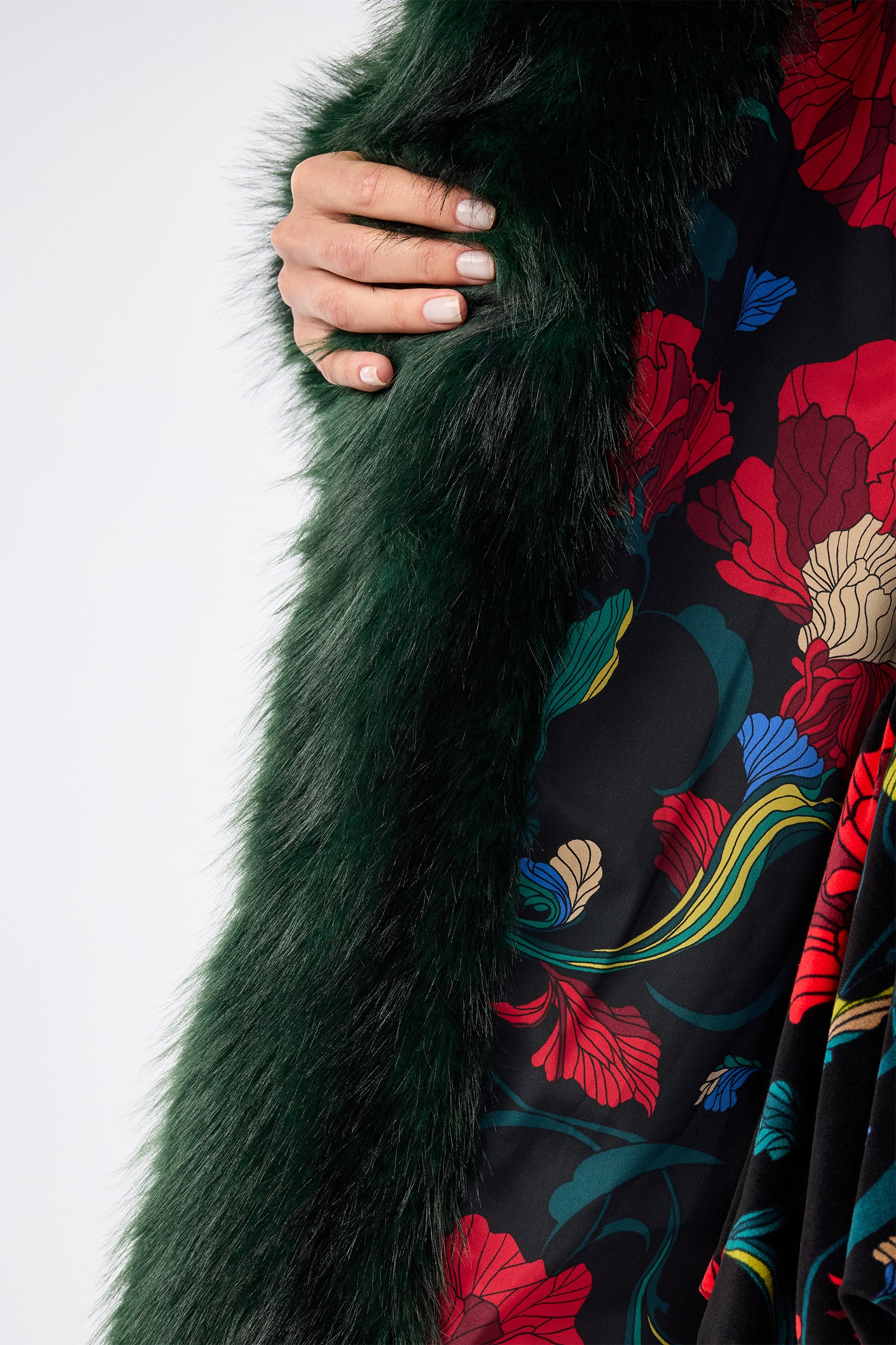 A person with manicured nails holds a dark green faux fur scarf while wearing the Dayos Coat, a black dress featuring vibrant red, blue, and beige floral patterns.