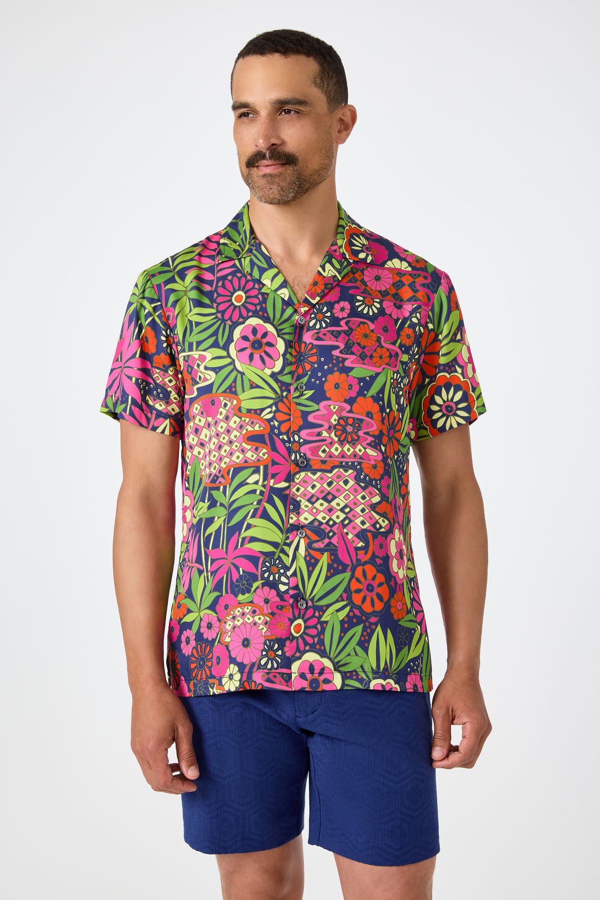 A man with short hair and a mustache wears the Felix Camp Shirt in Fumi Floral and dark blue shorts, standing against a plain white background.