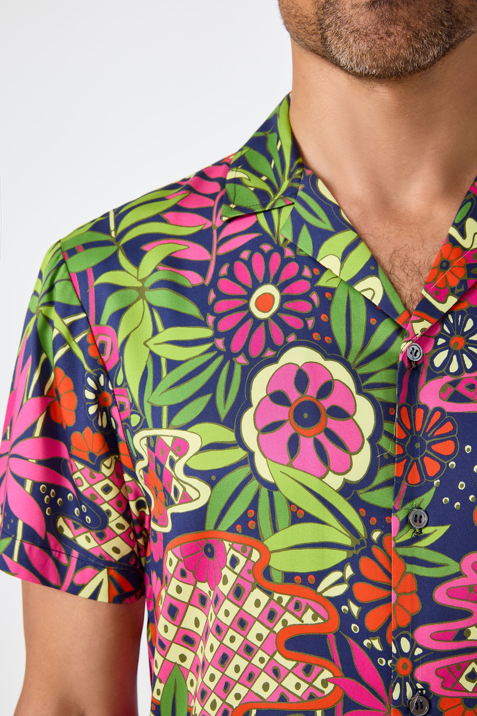 A man wears the Felix Camp Shirt - Fumi Floral, featuring vibrant pink, green, orange, and red floral patterns. Only his lower face and upper torso appear against a plain white background.
