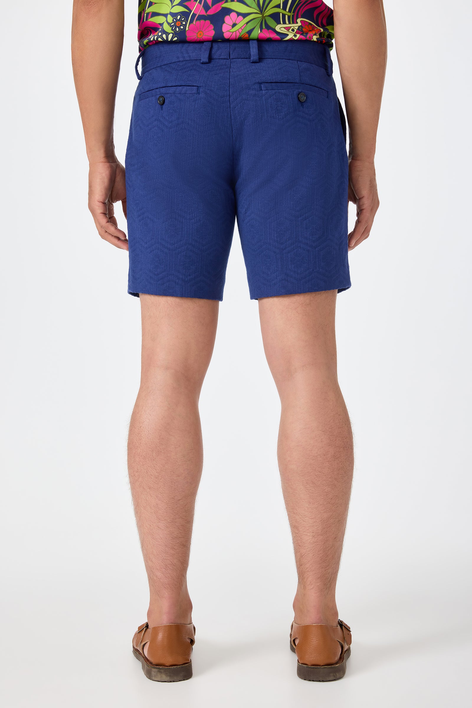 A person faces away, wearing the Lawrence Short - Noh Nightfall and a colorful floral shirt with brown sandals, set against a plain white background.