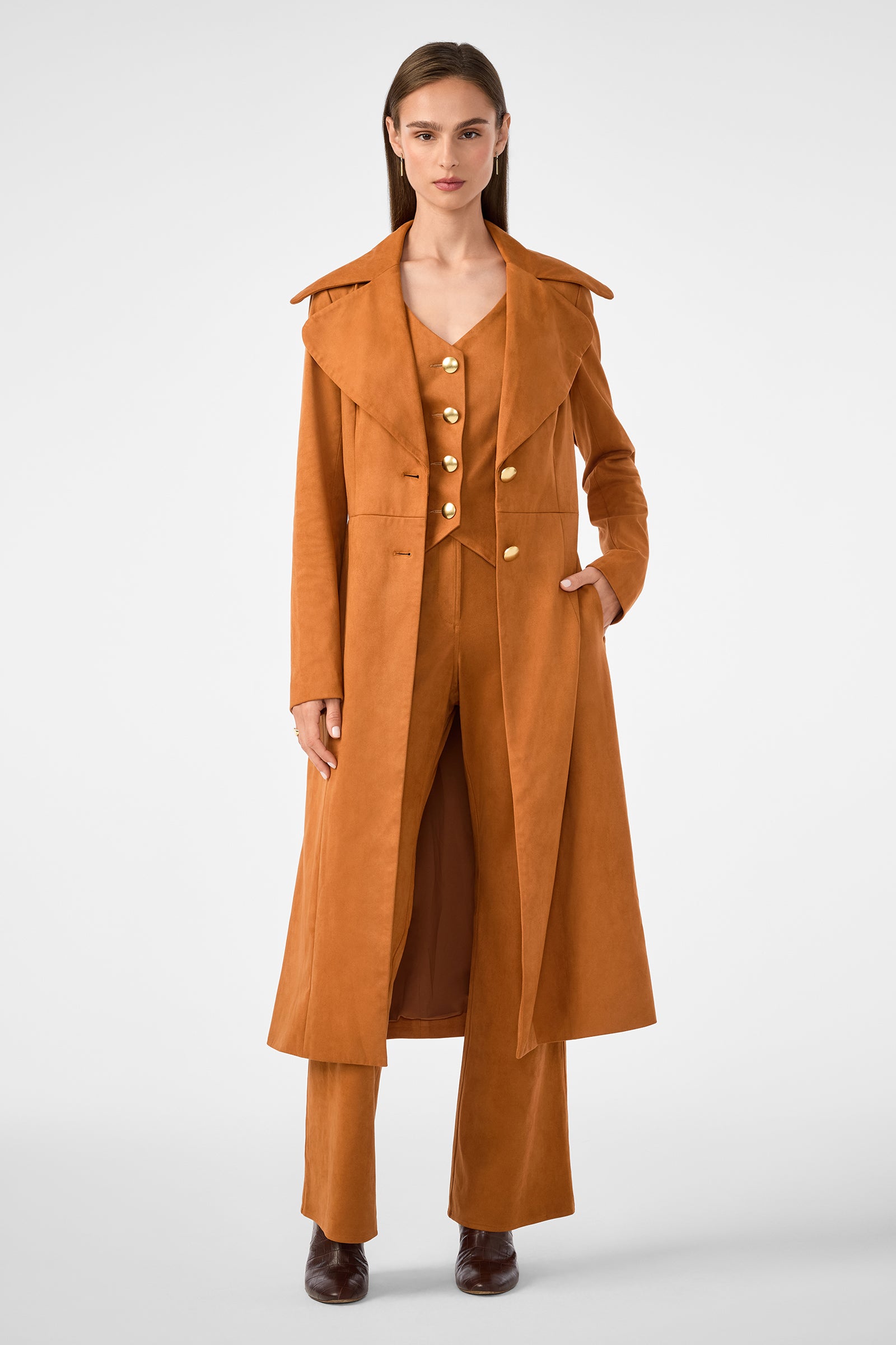 A woman faces forward in a rust suede coat over the Kofi 2 Vest and matching wide-leg pants. She has straight brown hair, brown shoes, and stands against a plain light background.